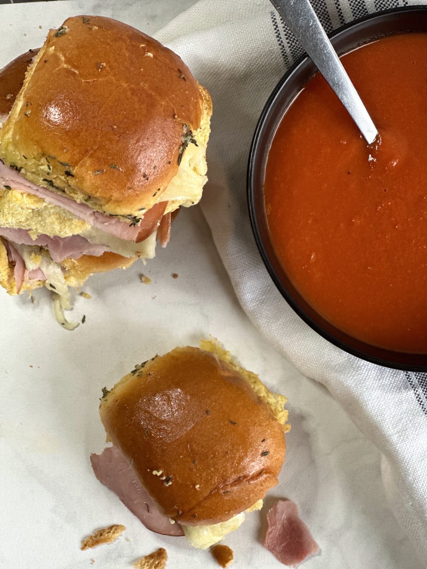 C1D153A9-0C31-41CE-A08B-7C655D09BB12 Hot ham and cheese sliders on golden buns seen from above with a bowl of homemade tomato soup.
