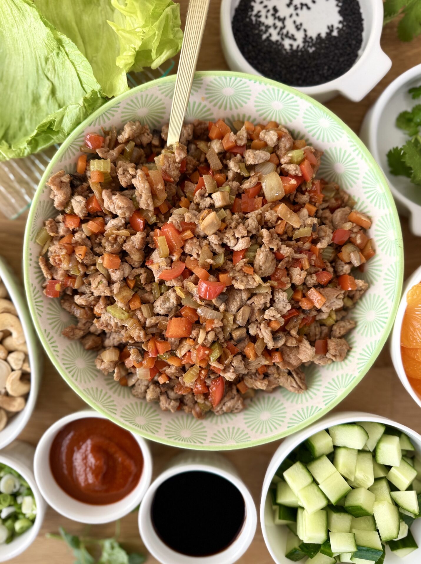 A bowl of Turkey Lettuce Wrap Filling is seen from above, surrounded by smaller bowls of colourful toppings for the wraps. 