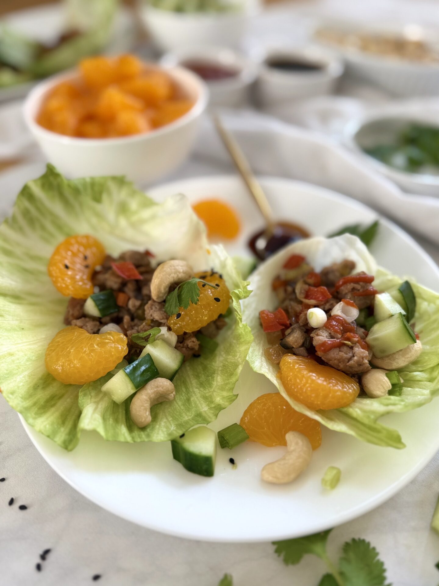 An individual dinner plate filed with a serving of turkey lettuce wraps is seen on a table, surrounded by small bowls of colourful toppings.