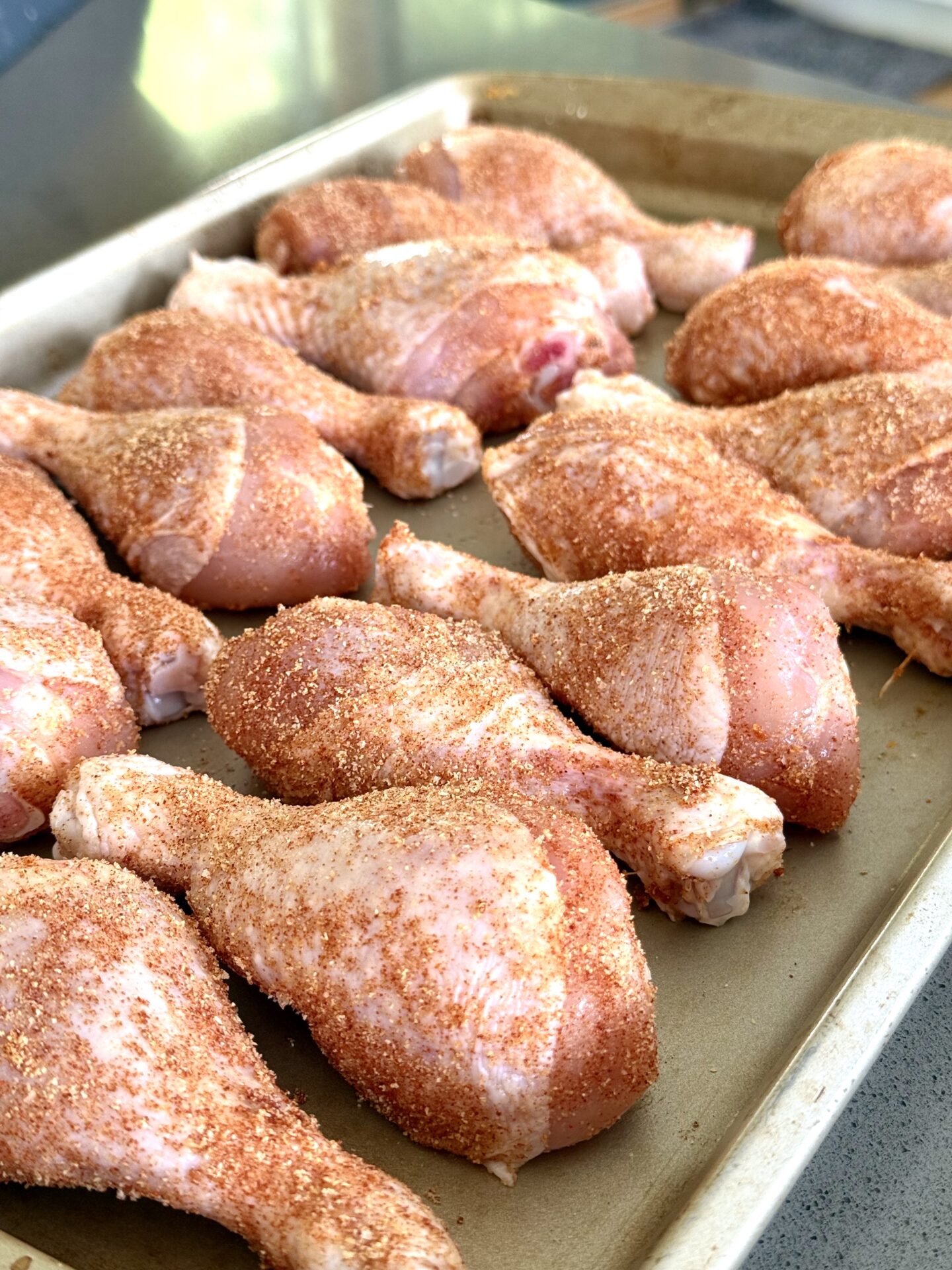 A tray of chicken legs coated in a dry rub sits on the counter, ready to be grilled.