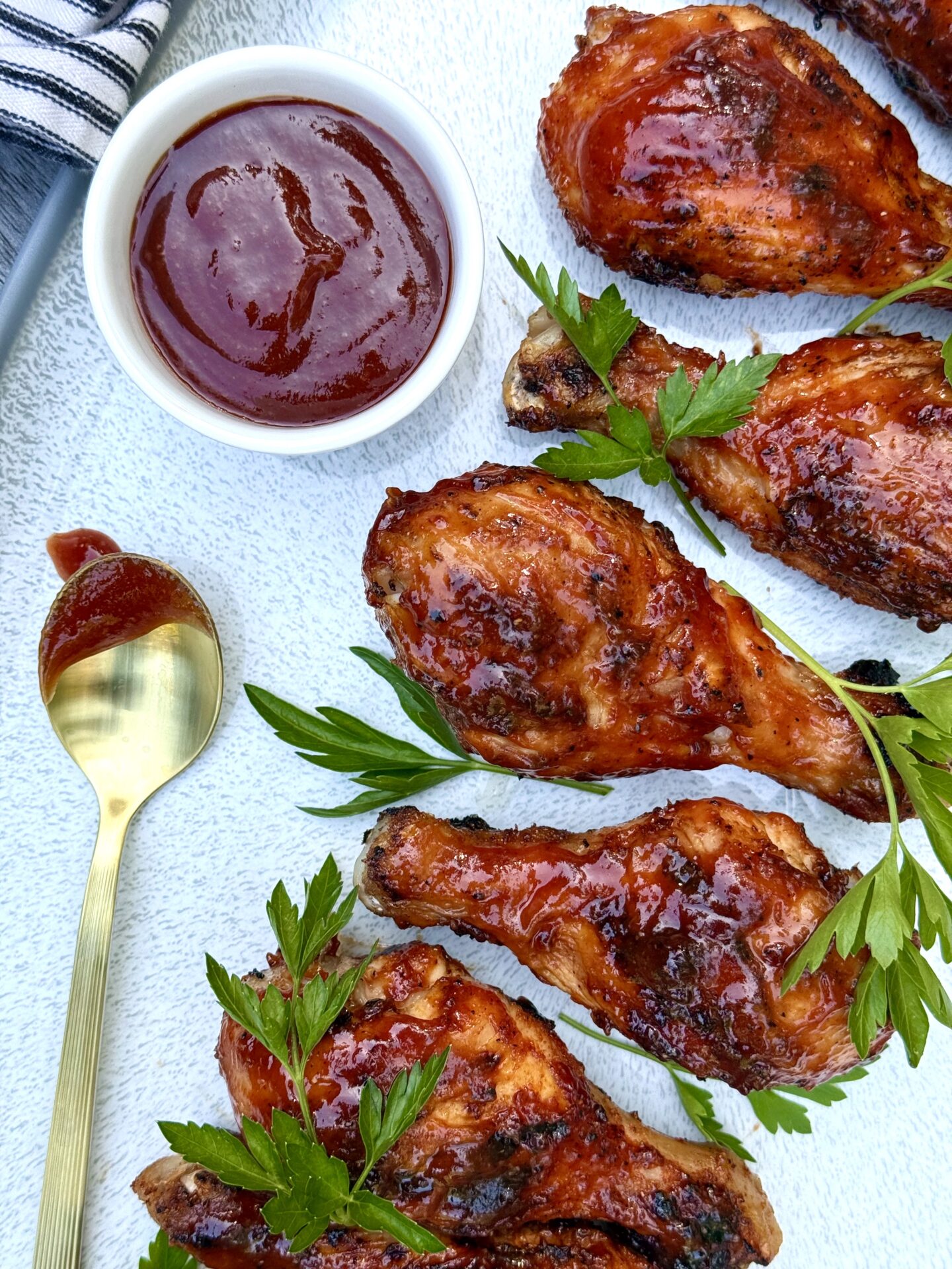 A platter of Smokey Sweet Grilled Chicken Legs is seen from above garnished with a dish of homemade barbecue sauce and fresh parsley.
