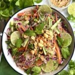 A vibrant bowl of Spring Roll Noodle Salad is seen from above, filled with colourful vegetables and topped with crushed peanuts, lime wheels and mint leaves.