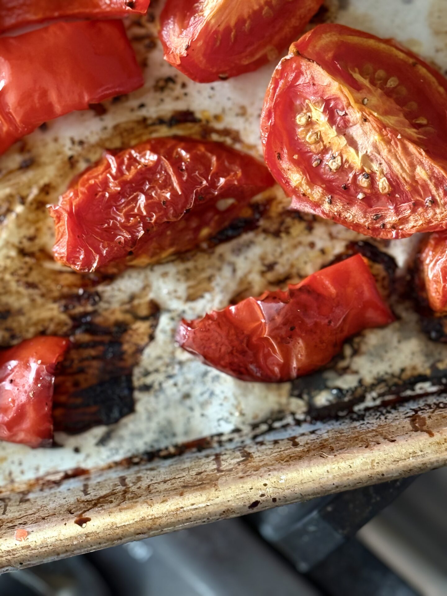 Roasted tomatoes and red peppers are seen close up, cooling on a baking sheet before being added to roasted tomato and feta soup.