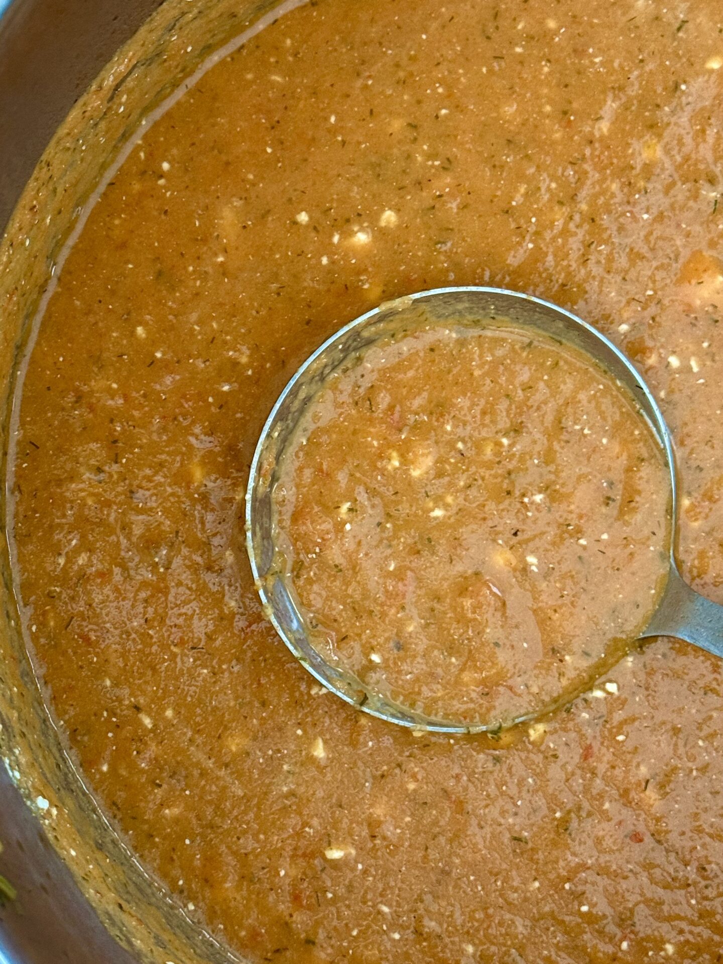 A ladle rests in a pot of Roasted Tomato and Feta soup, ready to serve.