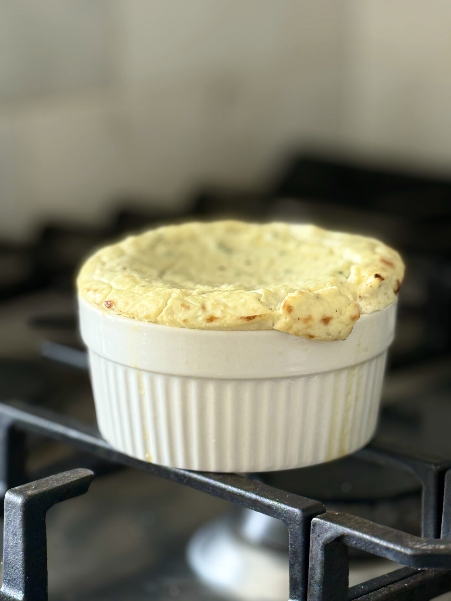 A baking dish of baked ricotta cools on a stove top. The image shows how the appetizer will rise in the oven like a soufflé, then sink in the centre as it cools.