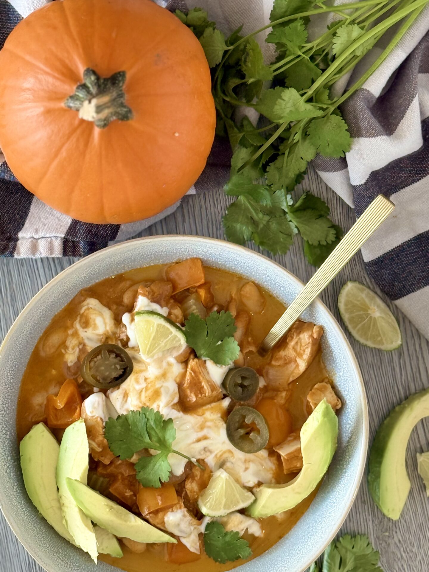 A bowl of lavishly garnished, orange coloured Creamy Pumpkin Chicken Chili is seen from above