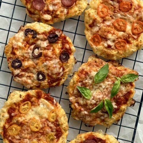 Cottage Cheese Pizza Buns featuring an assortment of toppings are seen from above, fresh from the oven, cooling on a black wire rack.