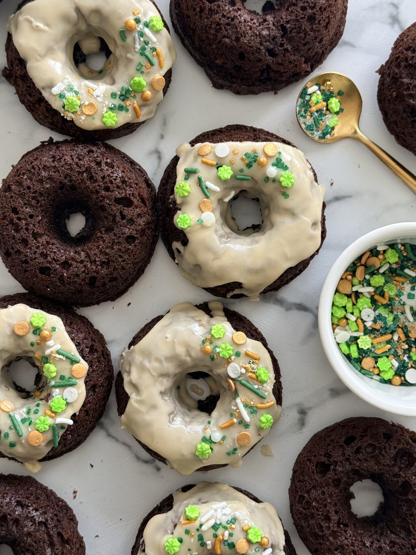 A group of chocolate donuts with Baileys glaze are seen from above garnished with festive sprinkles.