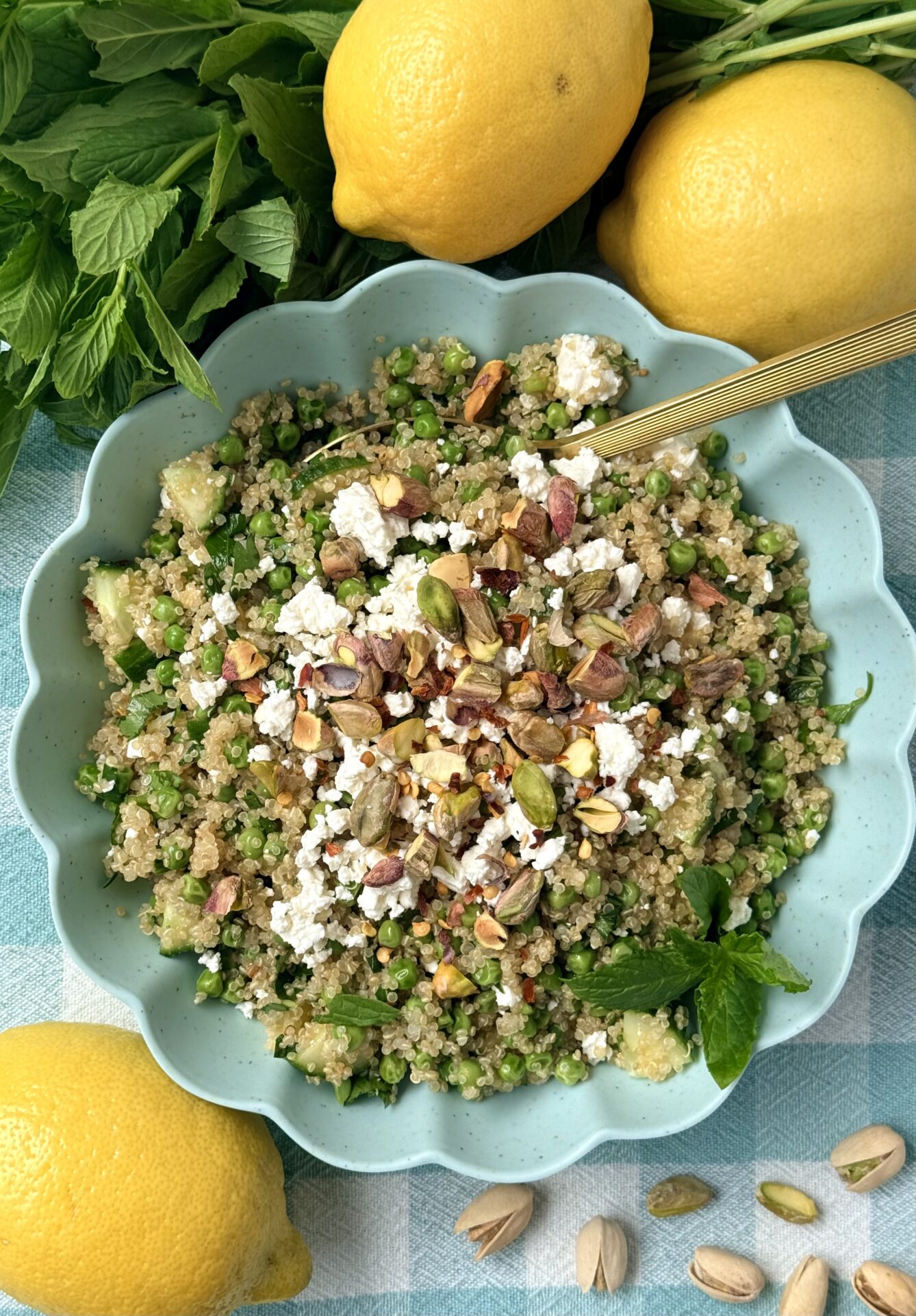 A bowl of lemony quinoa salad with peas, pistachios and mint is seen from above in a turquoise bowl.