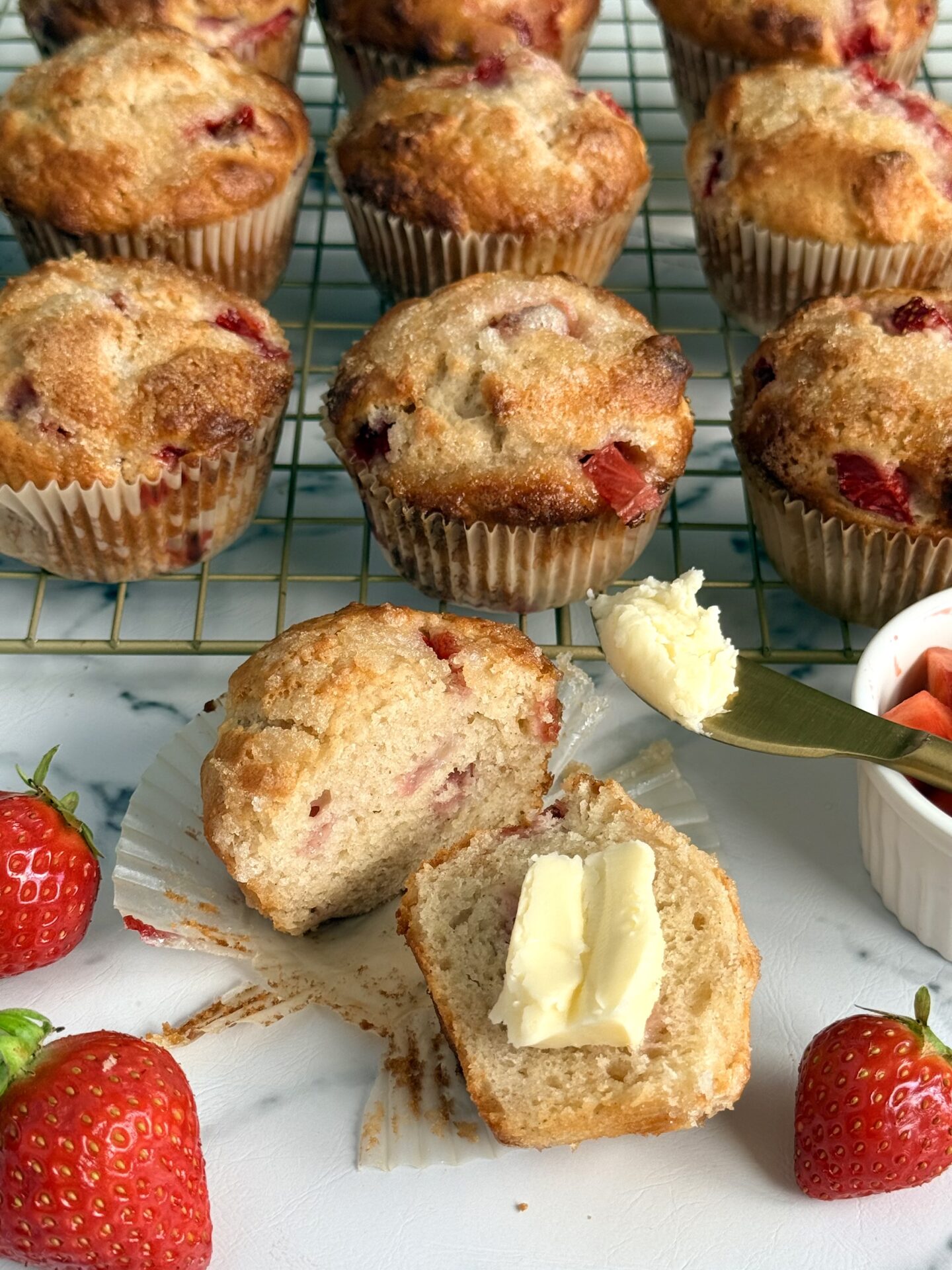 A strawberry yogurt muffin is split in two and slathered with butter.