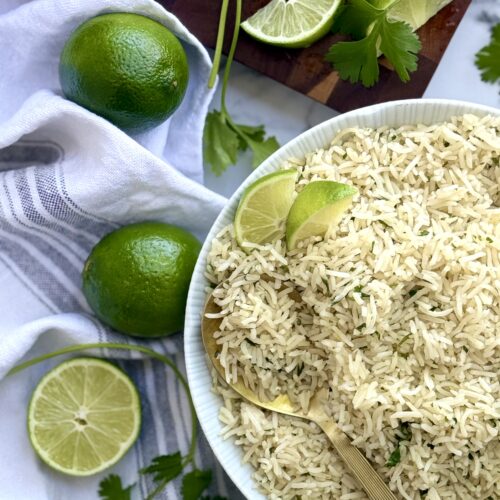 A bowl of cilantro lime rice is seen from above, surrounded by cut limes and fresh cilantro.