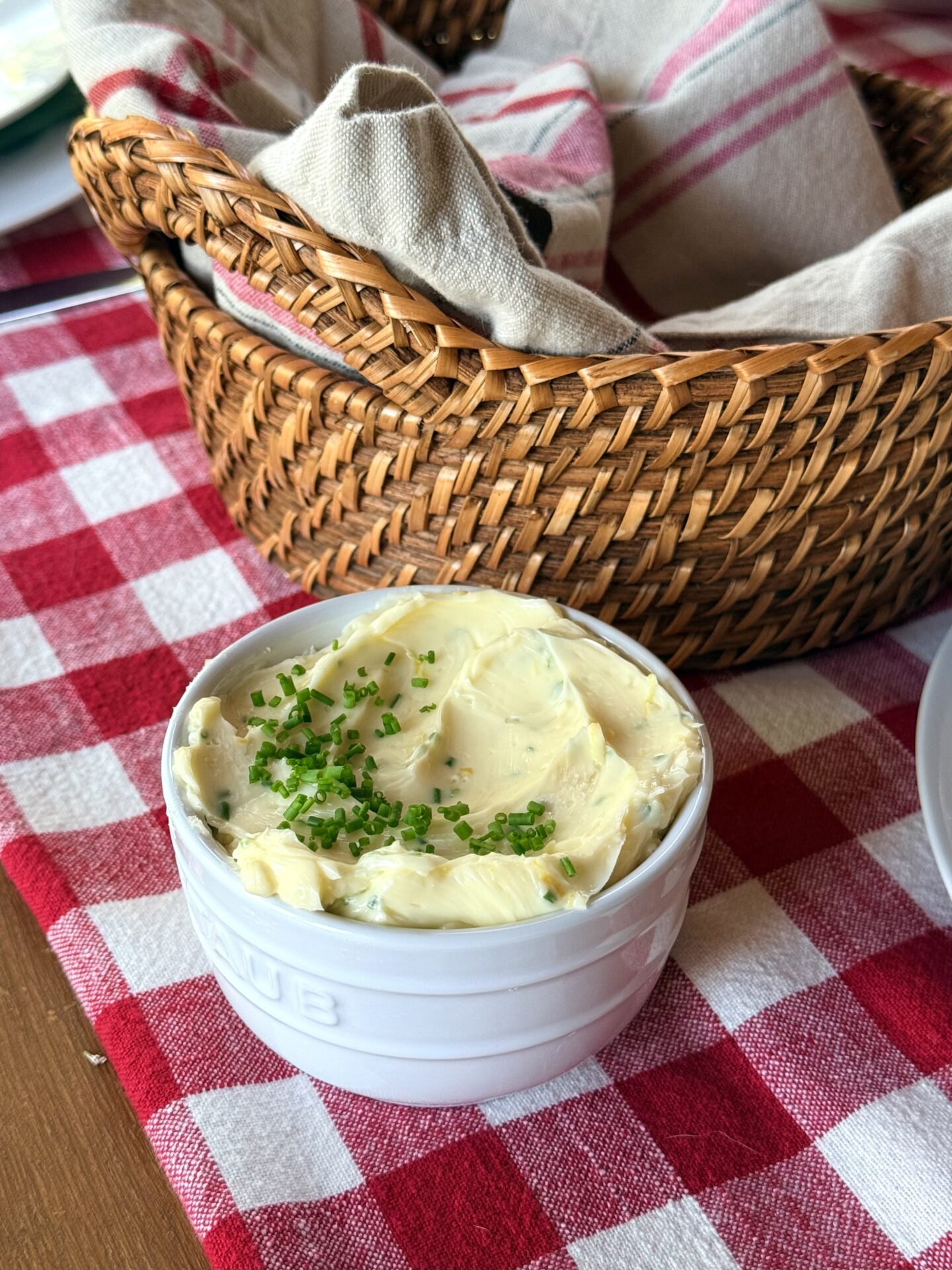 A small bowl of creamy lemon chive butter sits on a red gingham tablecloth