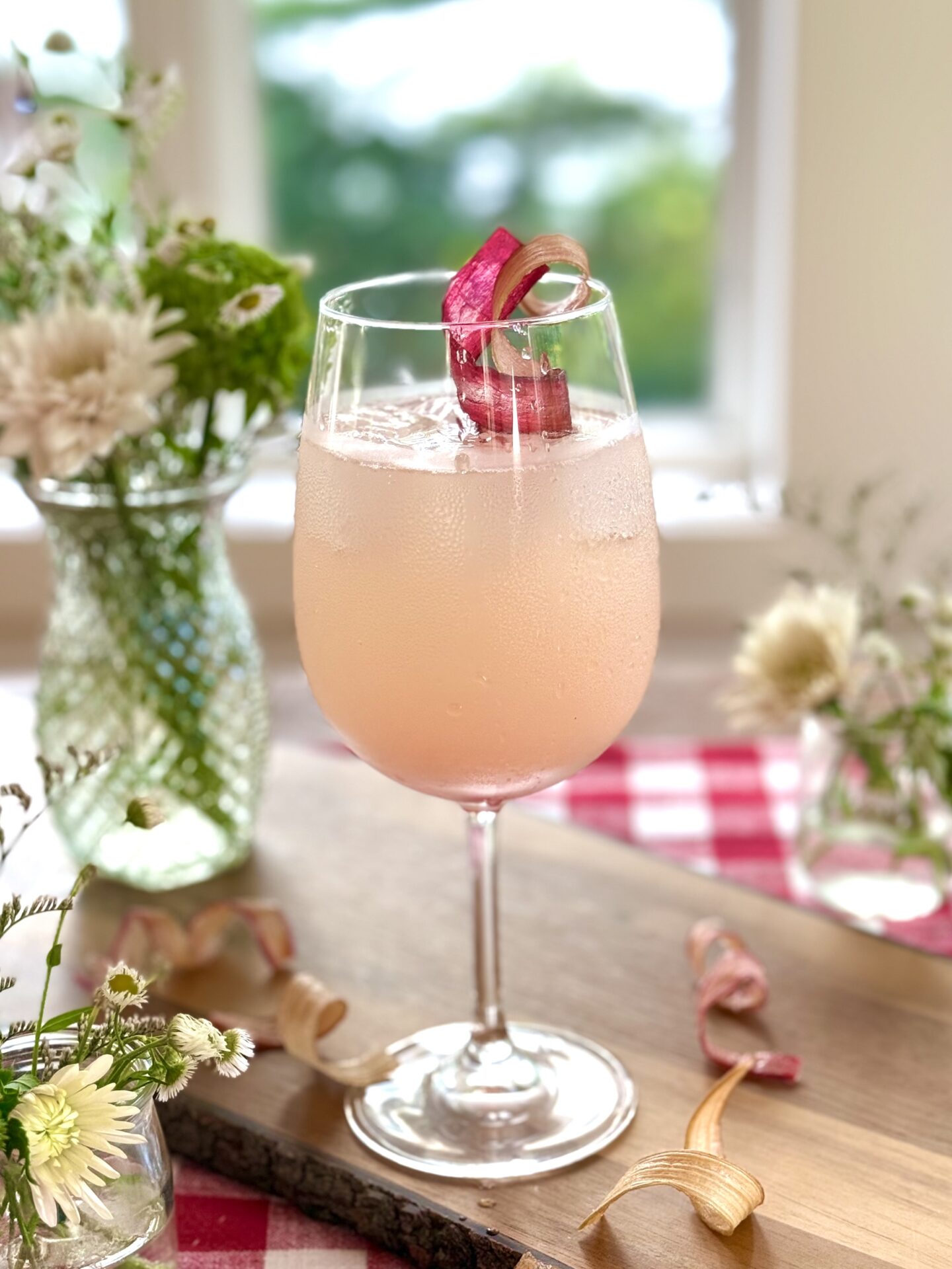A large glass filled with blush pink rhubarb gin spritz sits in front of a window