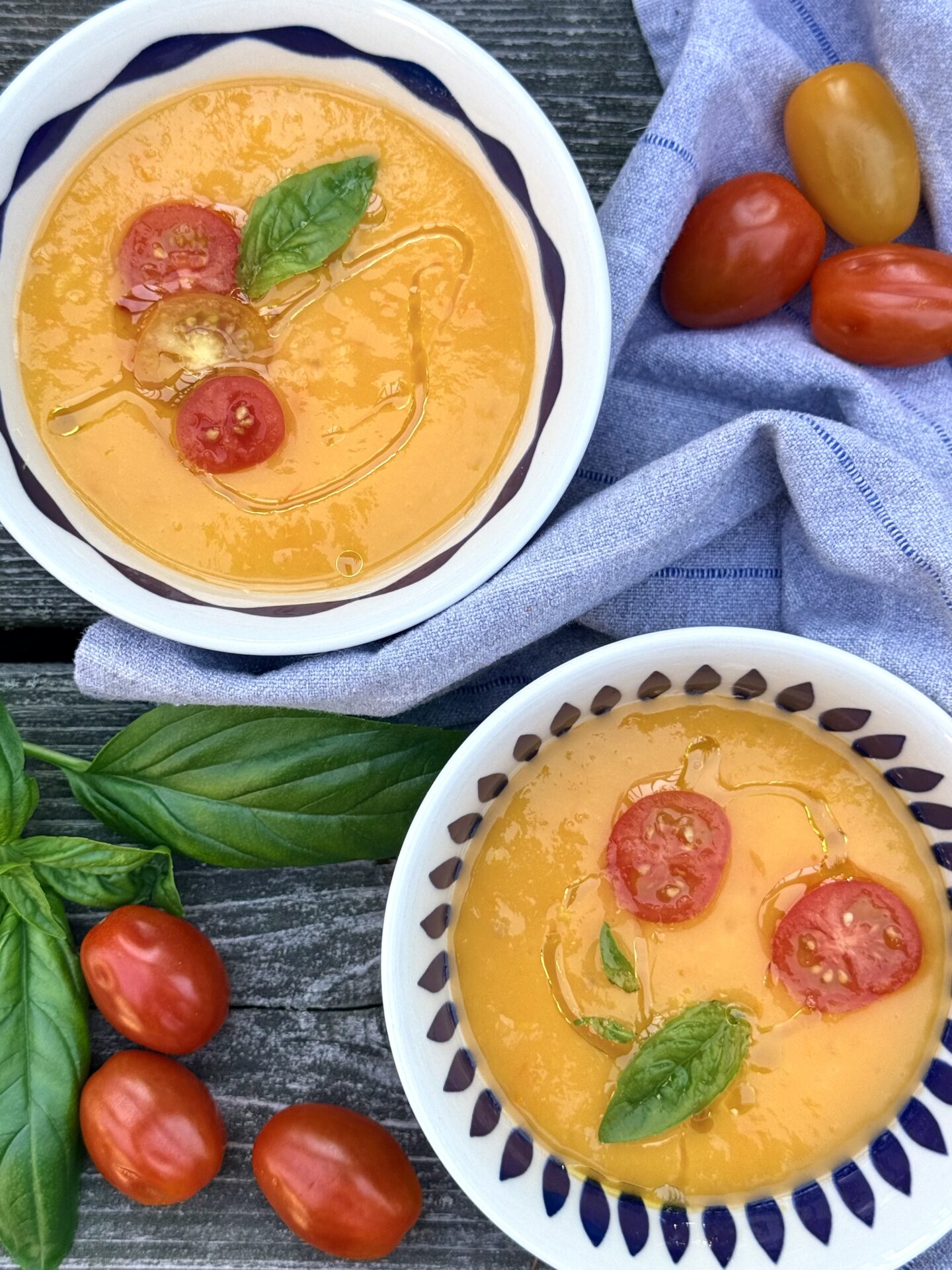 Bowls of Yellow Tomato Gazpacho are garnished with cherry tomatoes and basil.