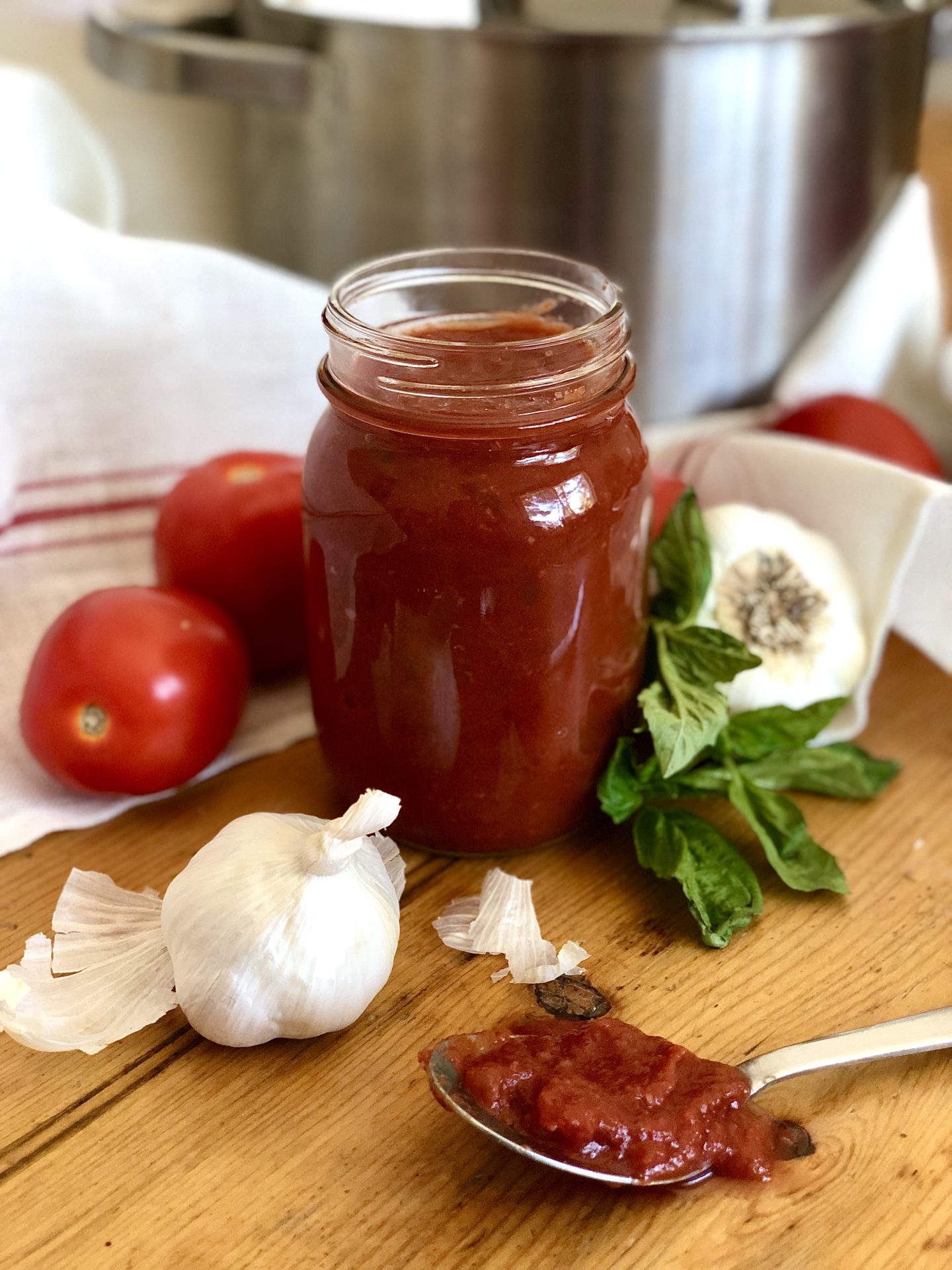 A jar of homemade marinara sauce sits on a wood cutting board surrounded by fresh garlic, tomatoes and basil