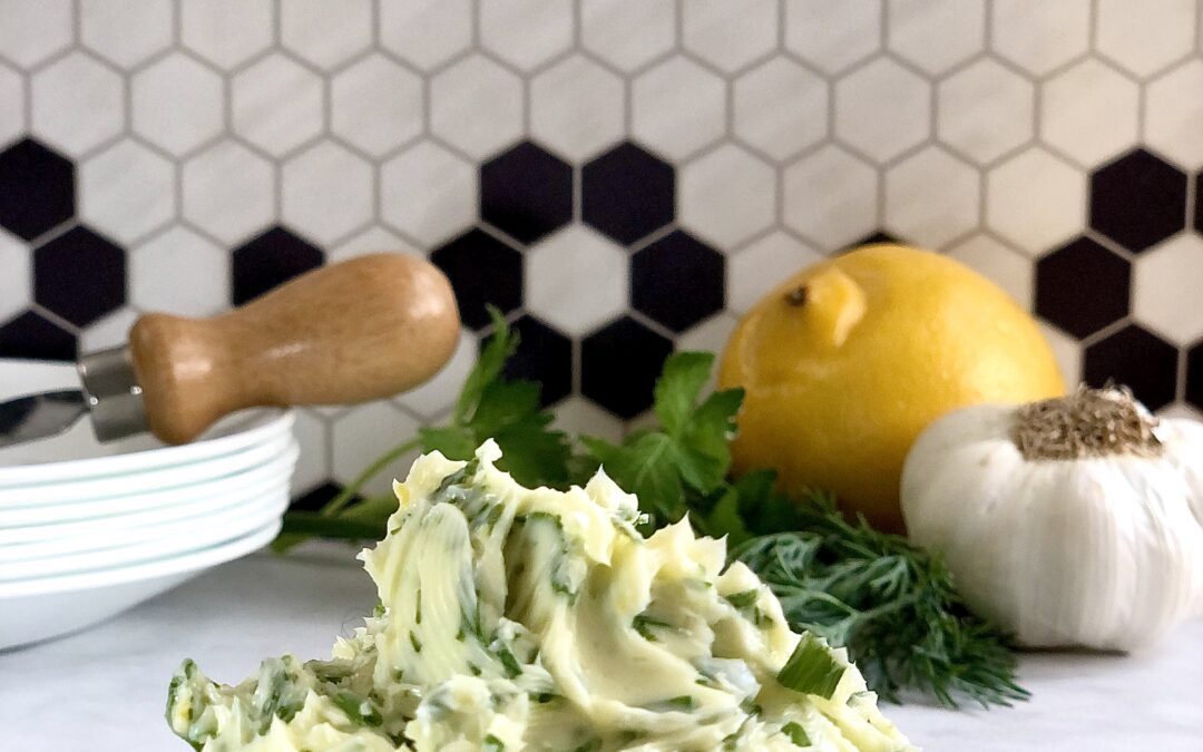 A dollop of creamy herb butter in a pretty dish, wet on a counter top with black and white backsplash tile