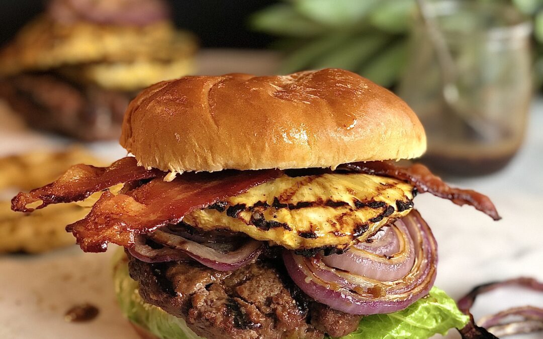 Burger topped with grilled pineapple, red onion slices and bacon with dripping sticky sweet rum sauce