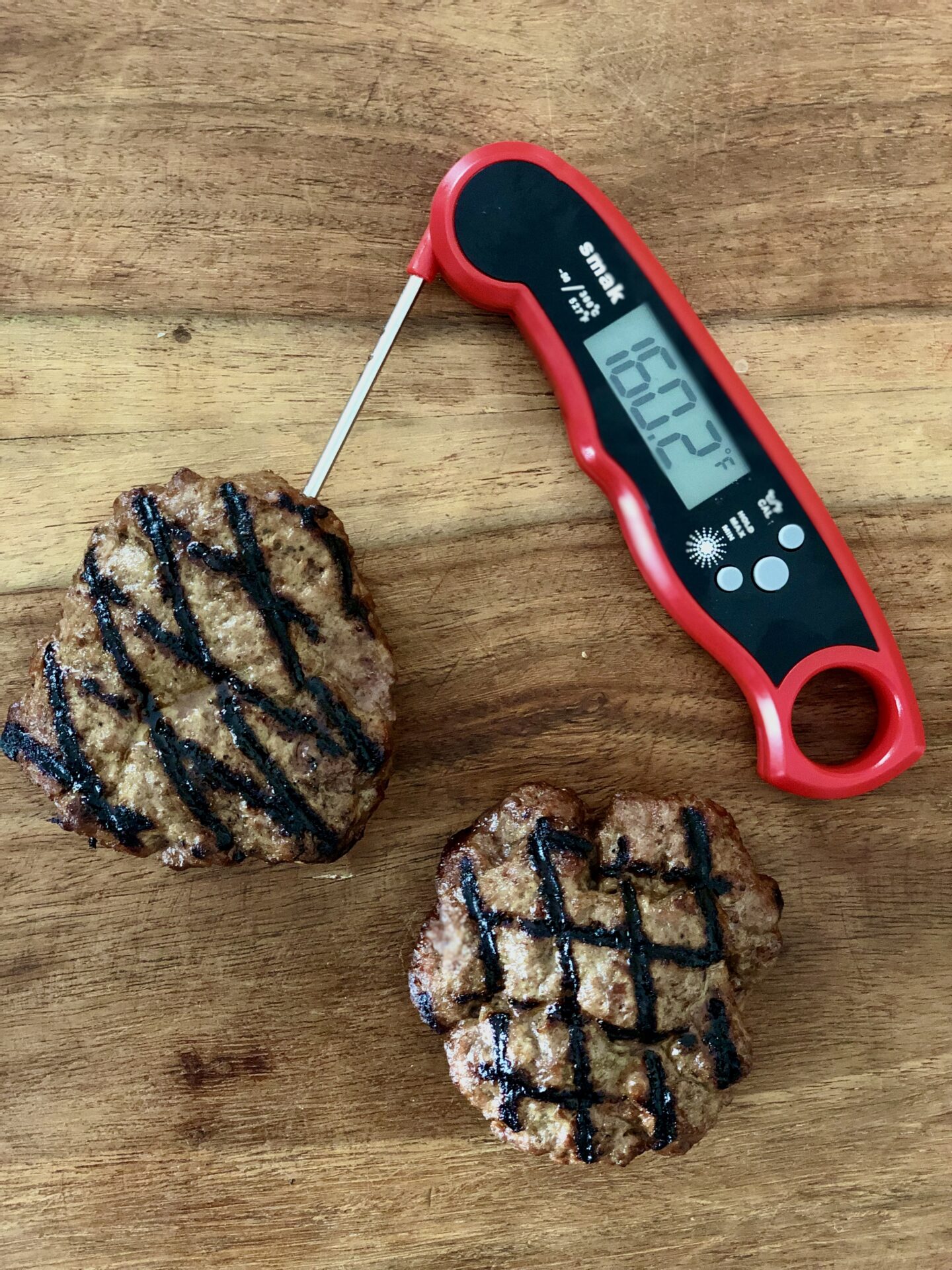 Grilled burger patties on a wood cutting board with instant read thermometer