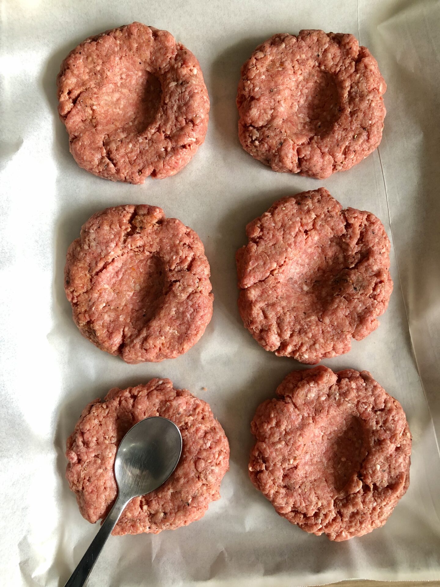 Uncooked beef burger patties on a tray with indentations