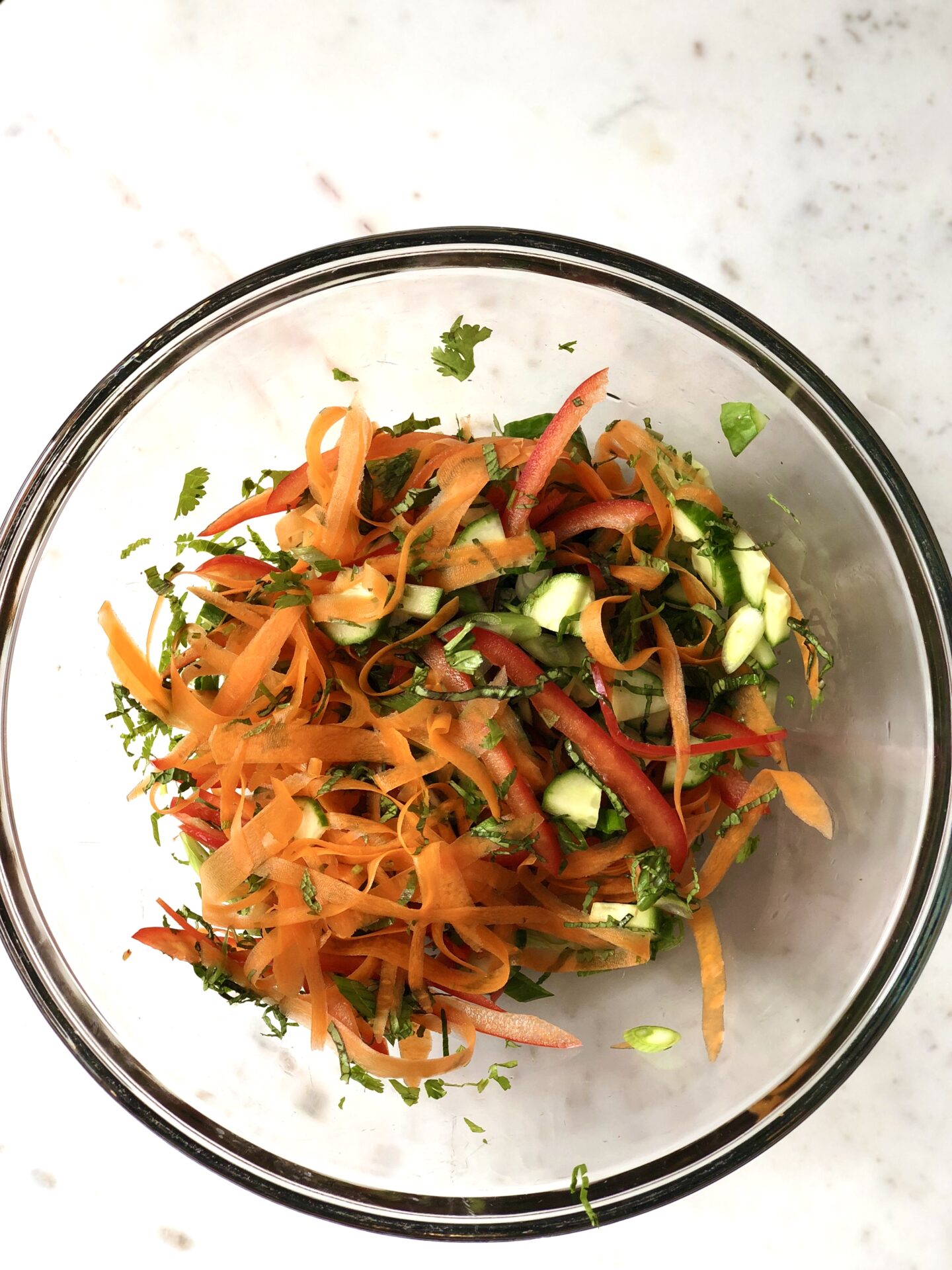 Cut vegetables and herbs tossed together in a glass bowl