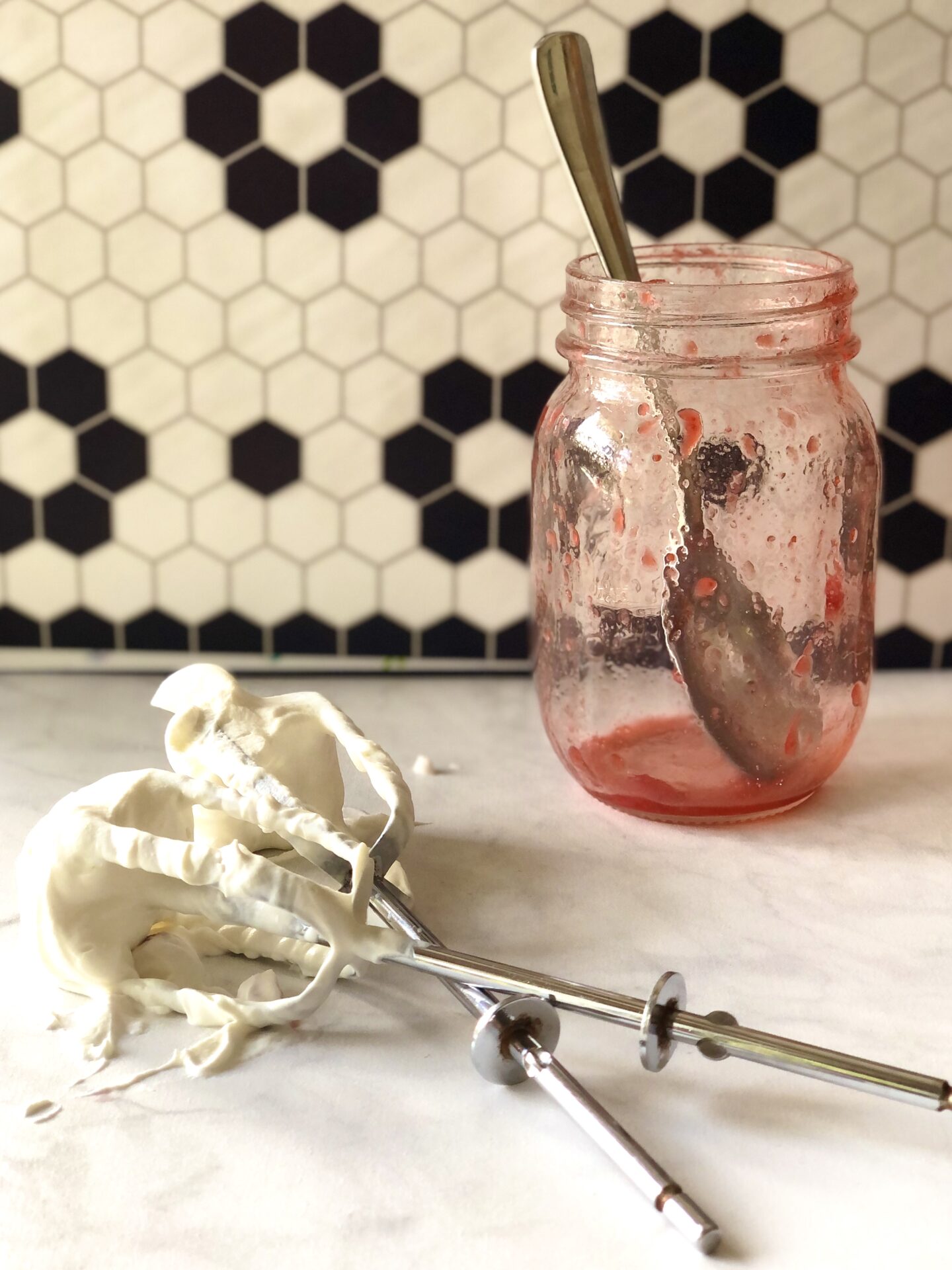 Empty strawberry sauce jar and beaters covered in whipped cream