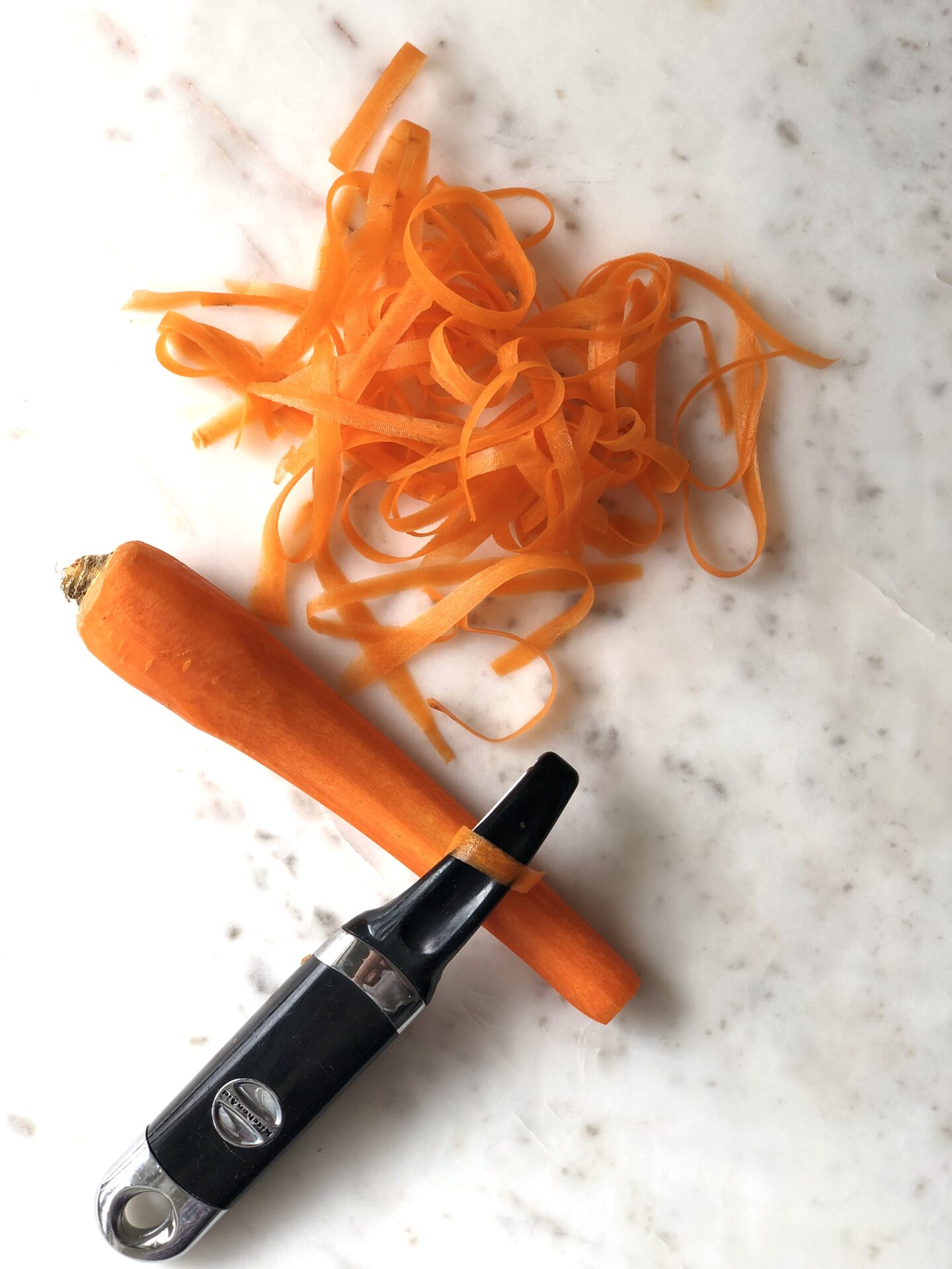 Carrot being cut into ribbons with a vegetable peeler