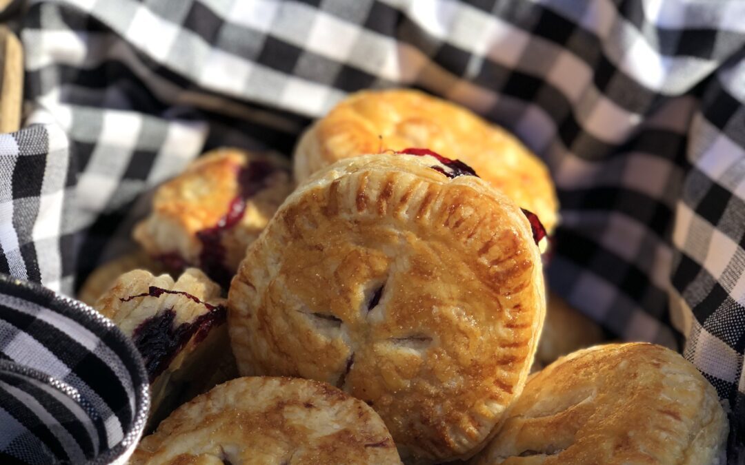 Golden pastry blueberry hand pies wrapped in gingham cloth at a picnic
