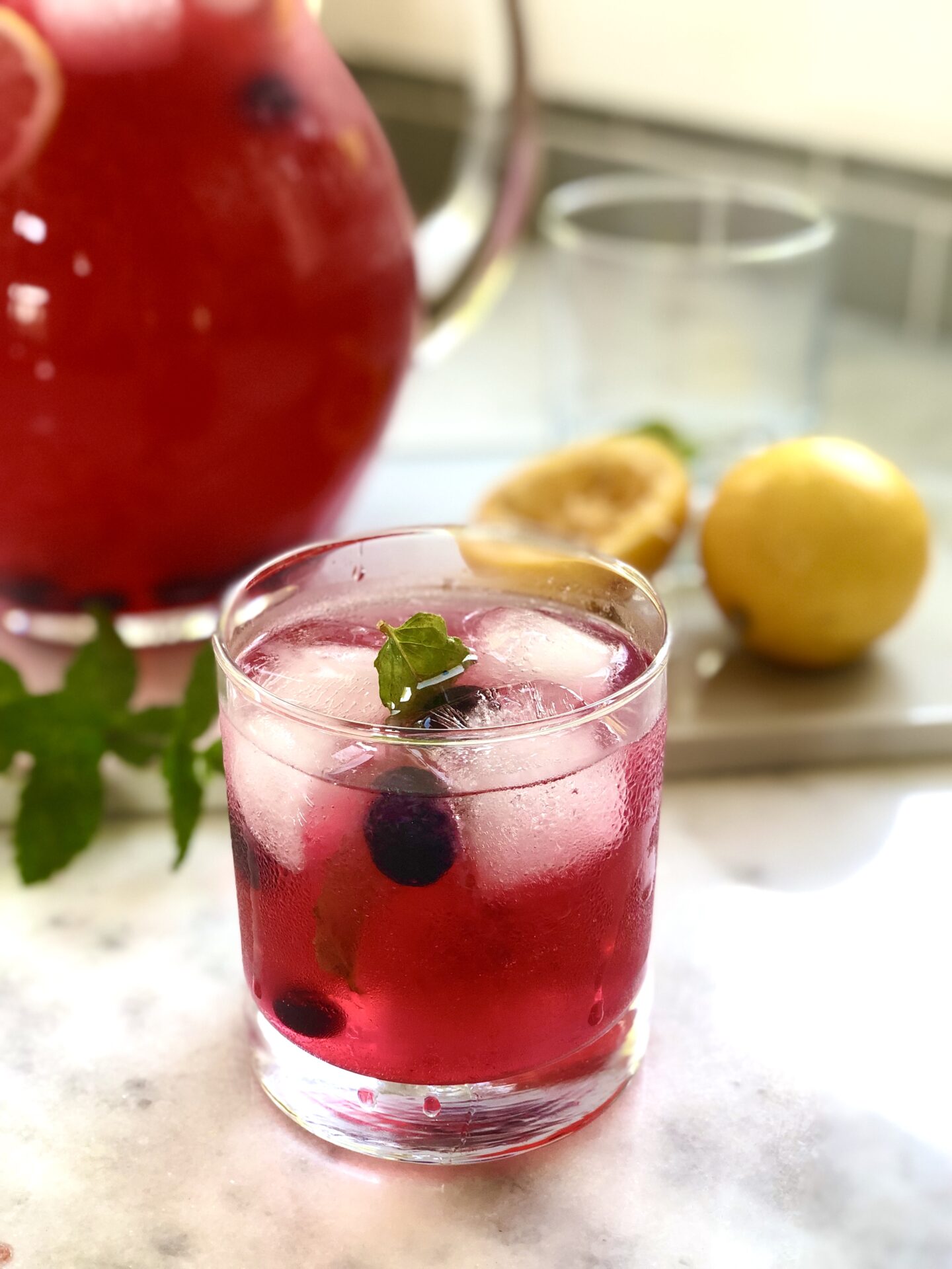 Glass filled with blueberry lavender lemonade garnished with ice blueberries and mint leaves