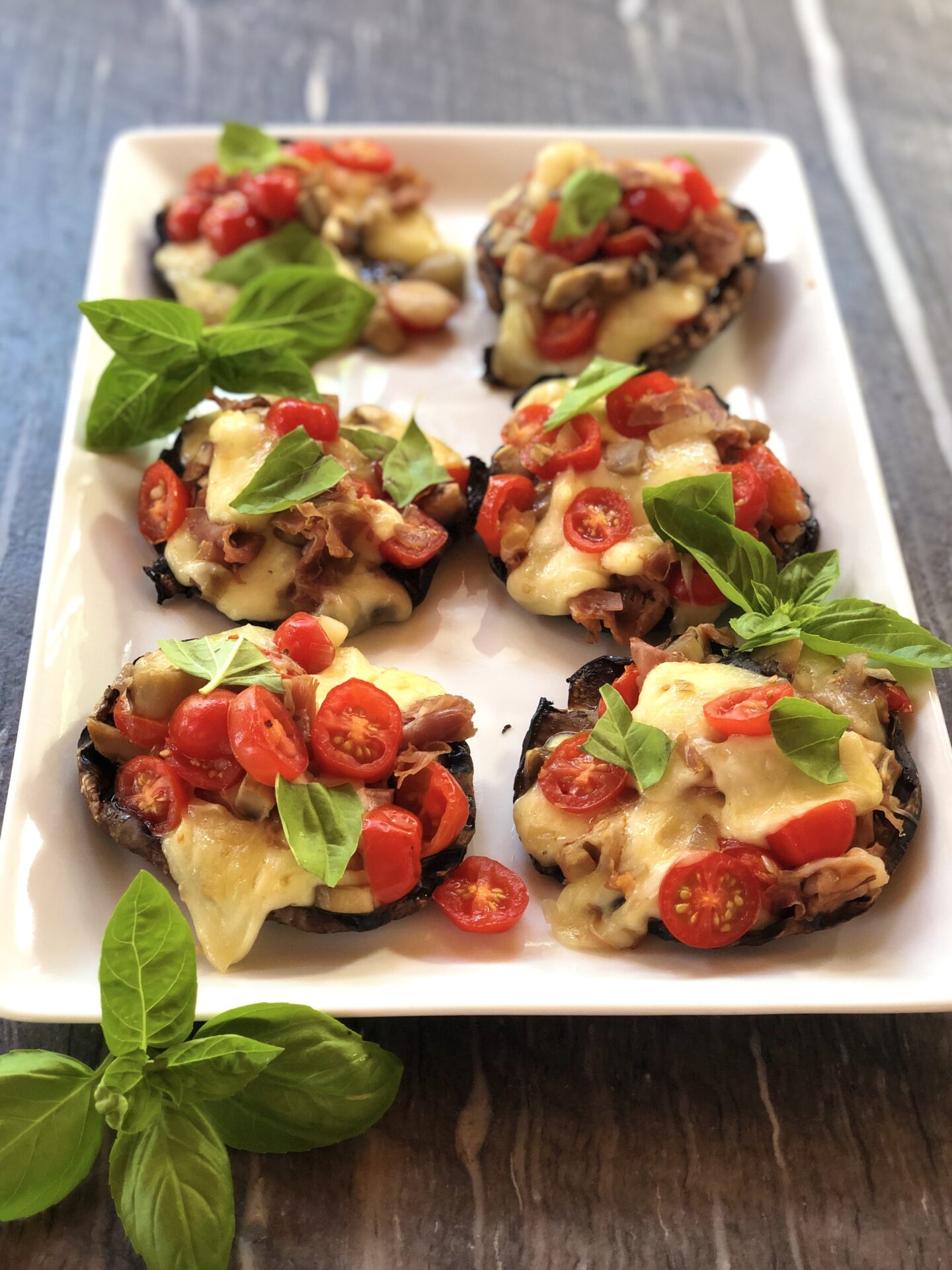Platter of grilled stuffed portobello mushrooms with cheese, tomato and fresh basil