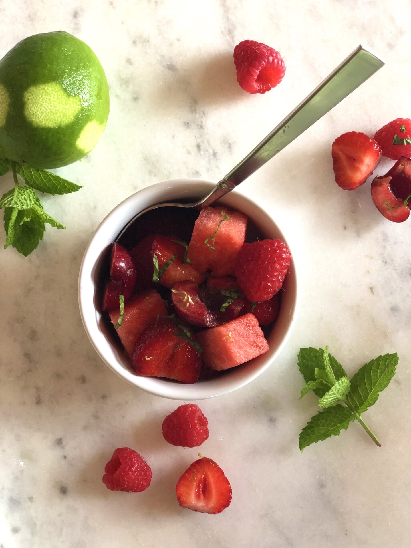 Small bowl of red fruit salad with berries lime and mint