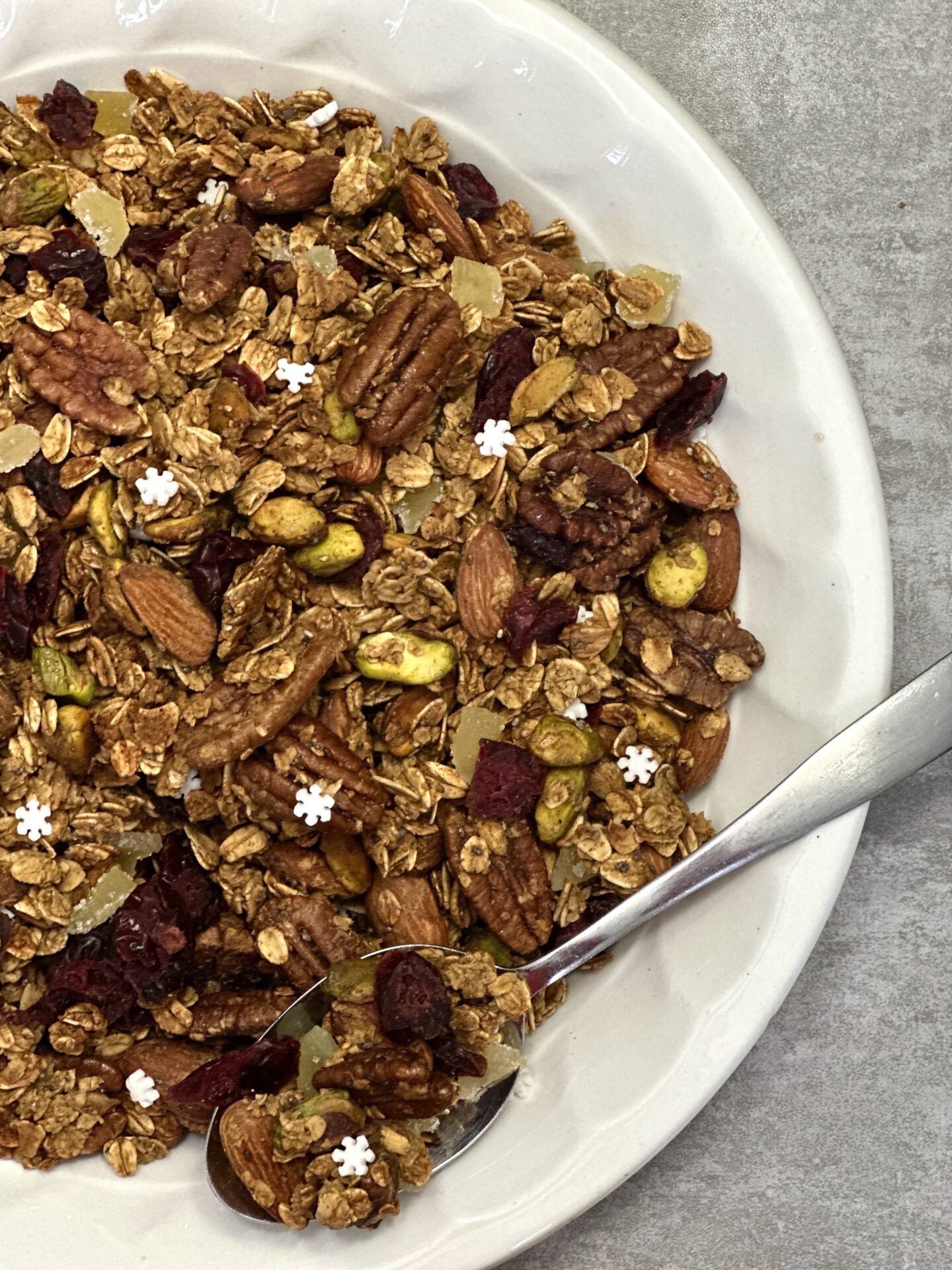 Bowl of homemade gingerbread granola with pecans almonds pistachios cranberries pears candied ginger and snowflake sprinkles