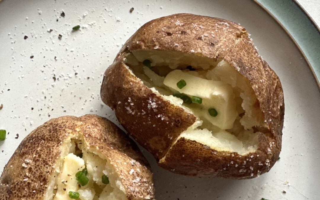Two perfect baked potatoes split open and topped with pats of butter and sprinkled with chives
