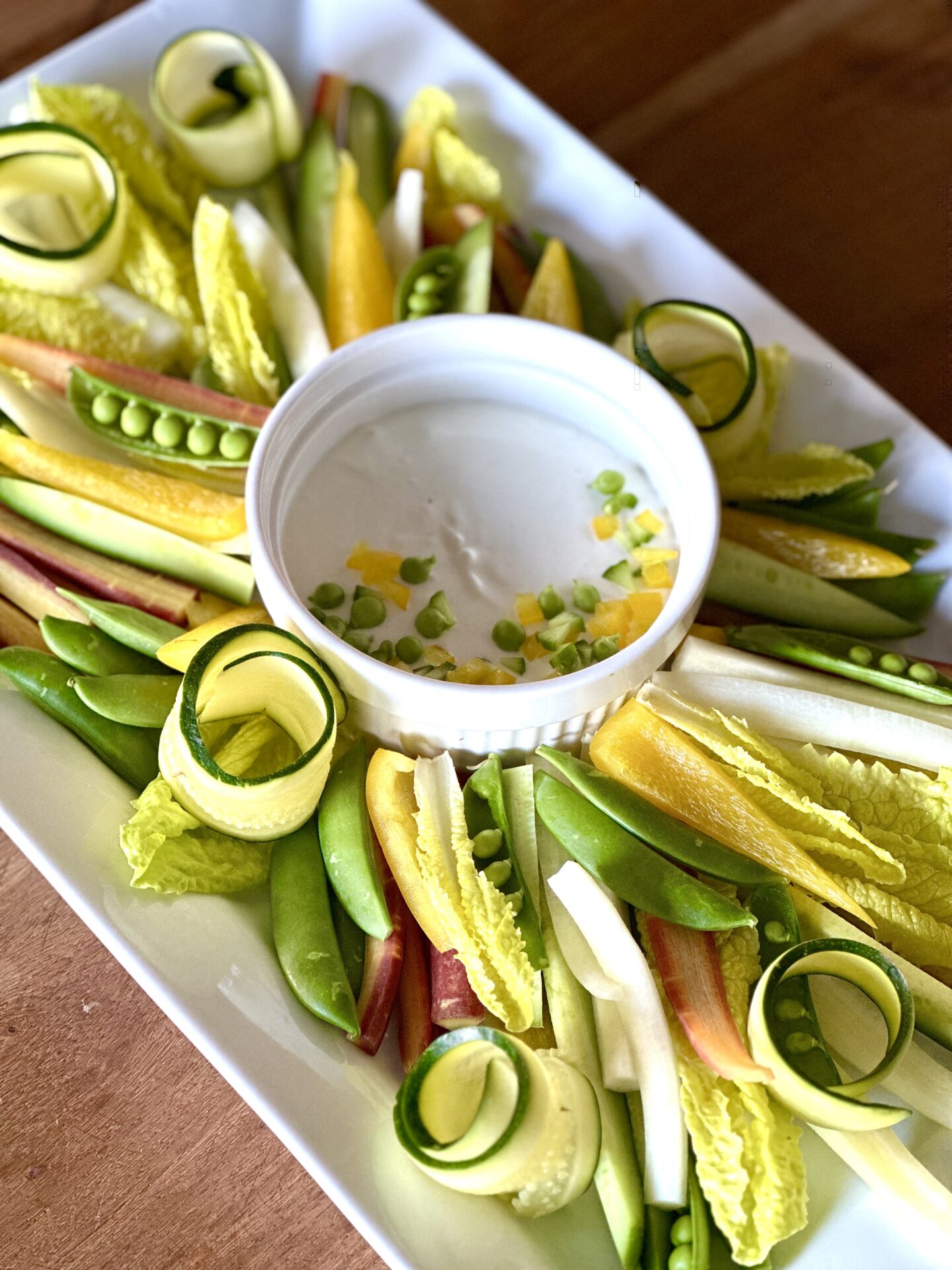 Platter of fresh spring peas, carrots, lettuce, peppers and zucchini with a light and creamy lemon dip