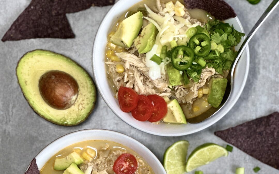 Bowls of White Chicken Chili surrounded by blue corn tortilla chips, avocado, fresh jalapeños and sliced scallions