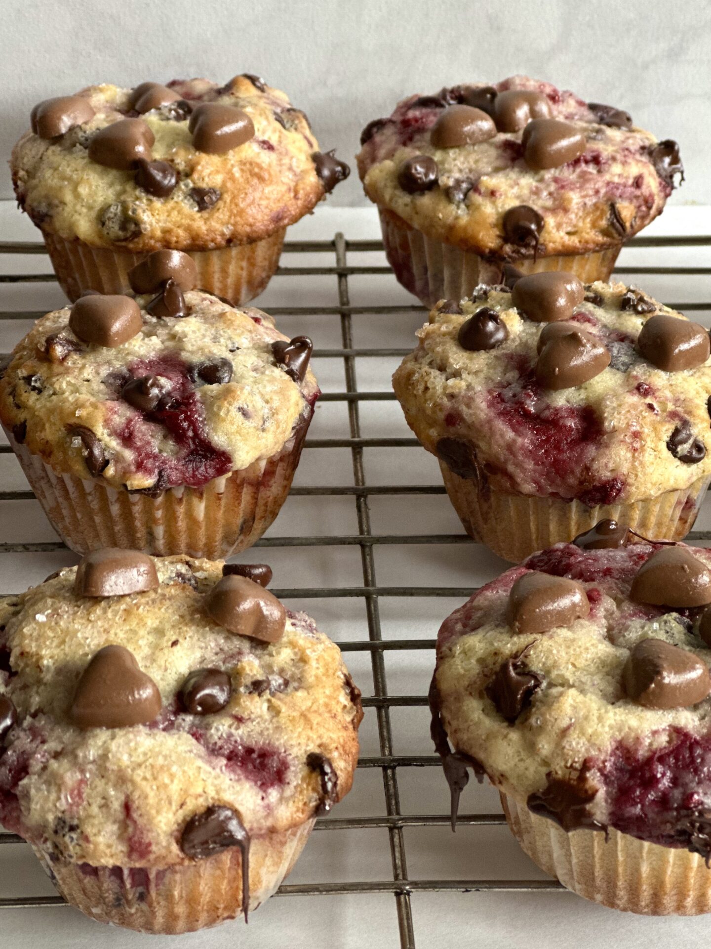 A batch of fresh warm raspberry chocolate chip muffins, decorated with hearts for valentines day, seen cooling on a rack.