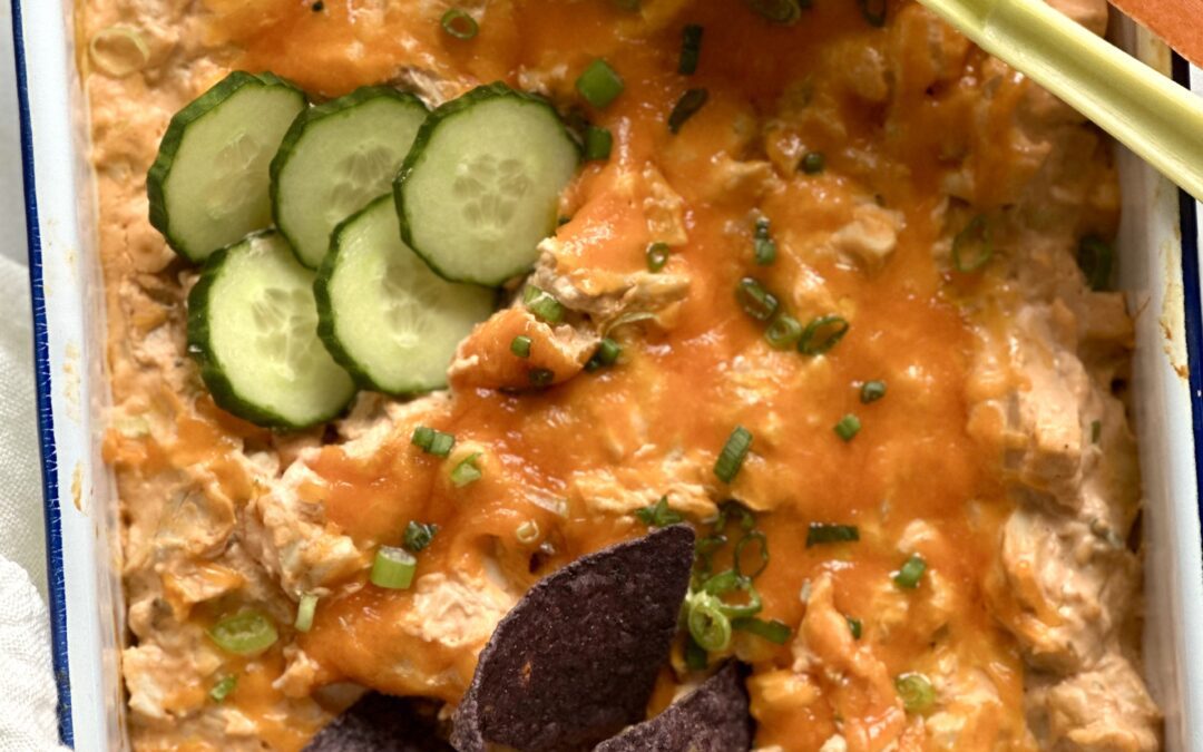 White enamel pan of Hot and Spicy Buffalo Chicken Dip with blue corn chips and vegetables for scooping.