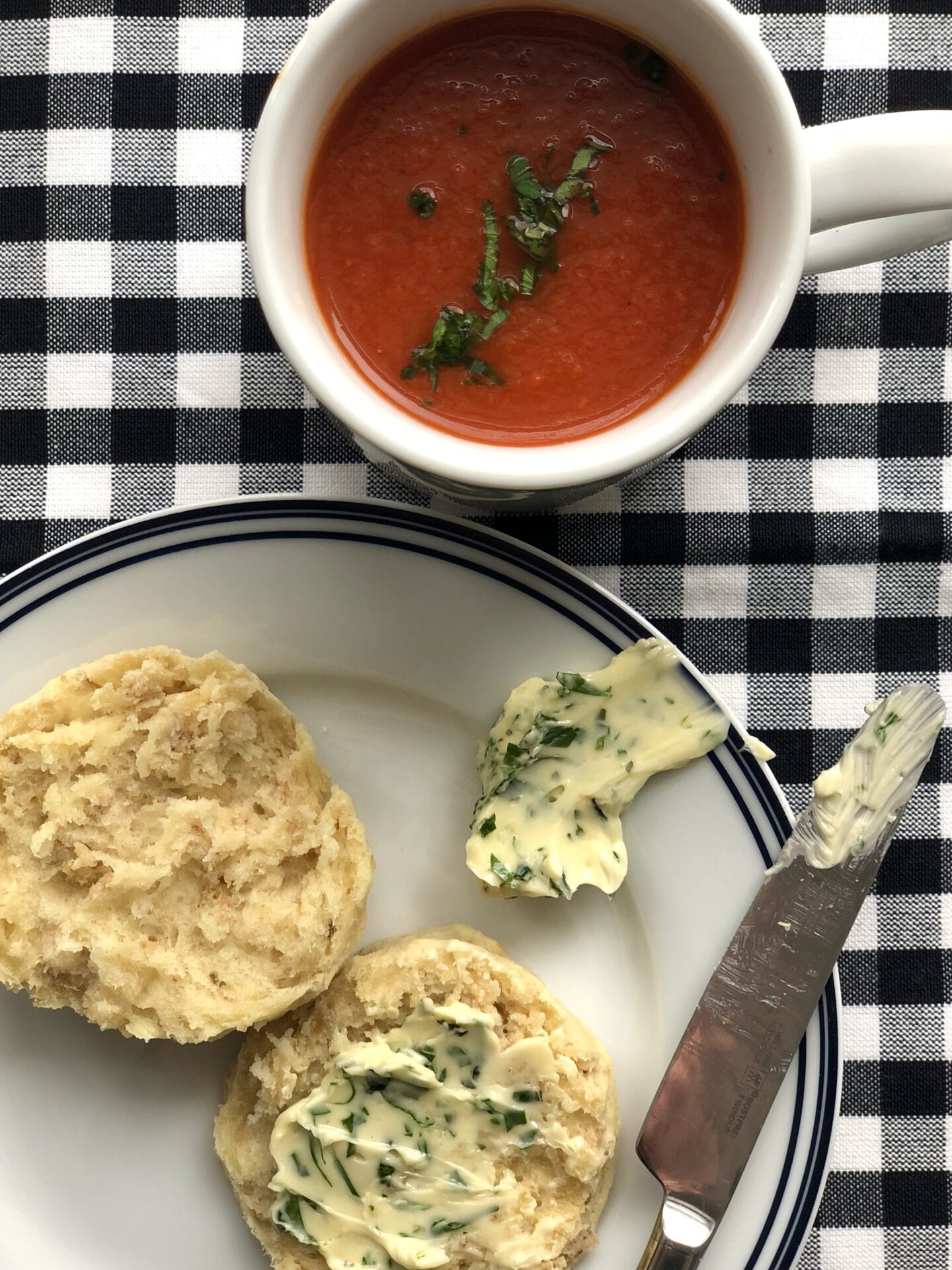 A mug of homemade tomato soup with a warm biscuit and herb butter