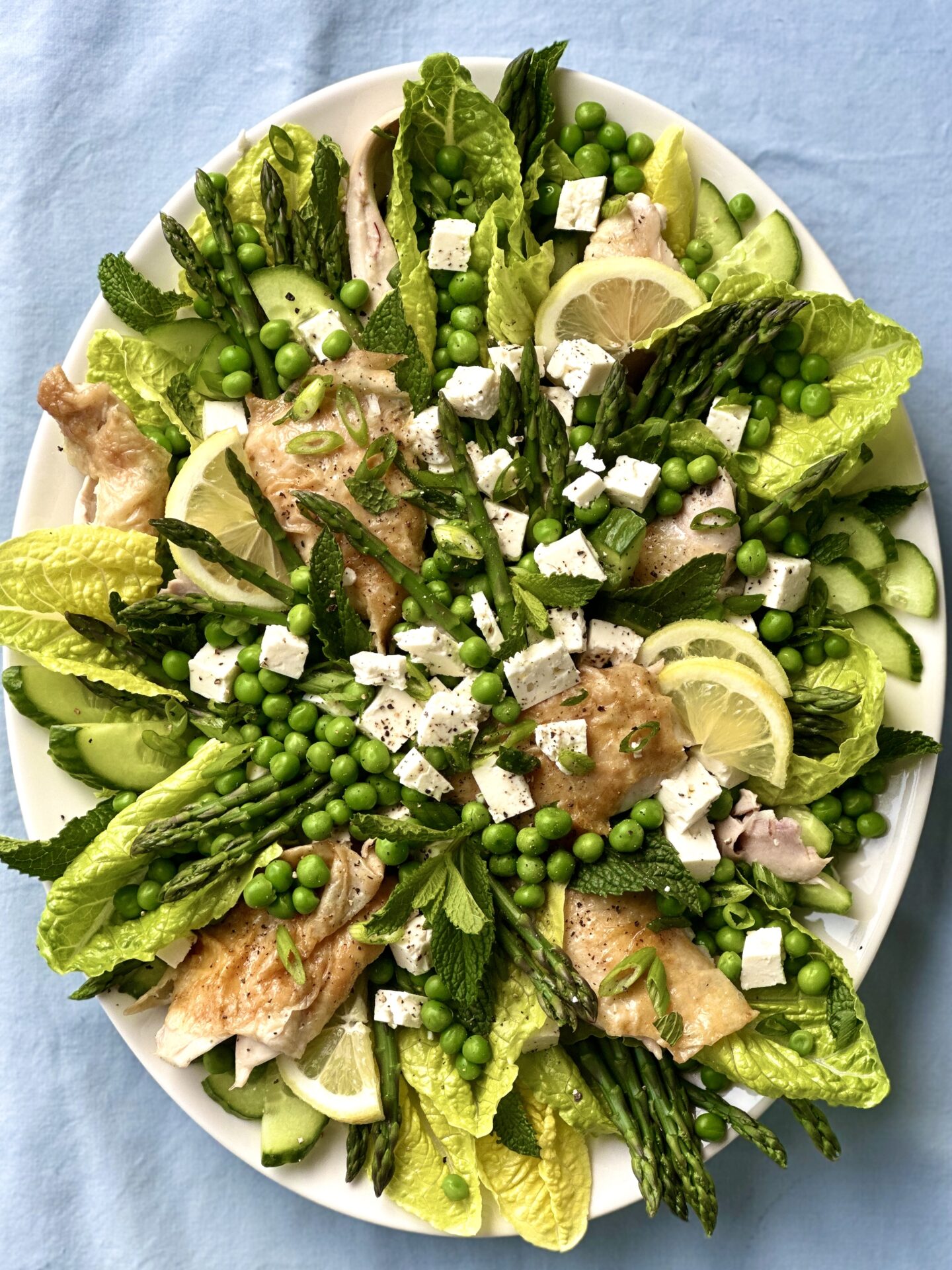 Platter of beautifully arranged salad greens with peas, asparagus, roast chicken and feta cheese