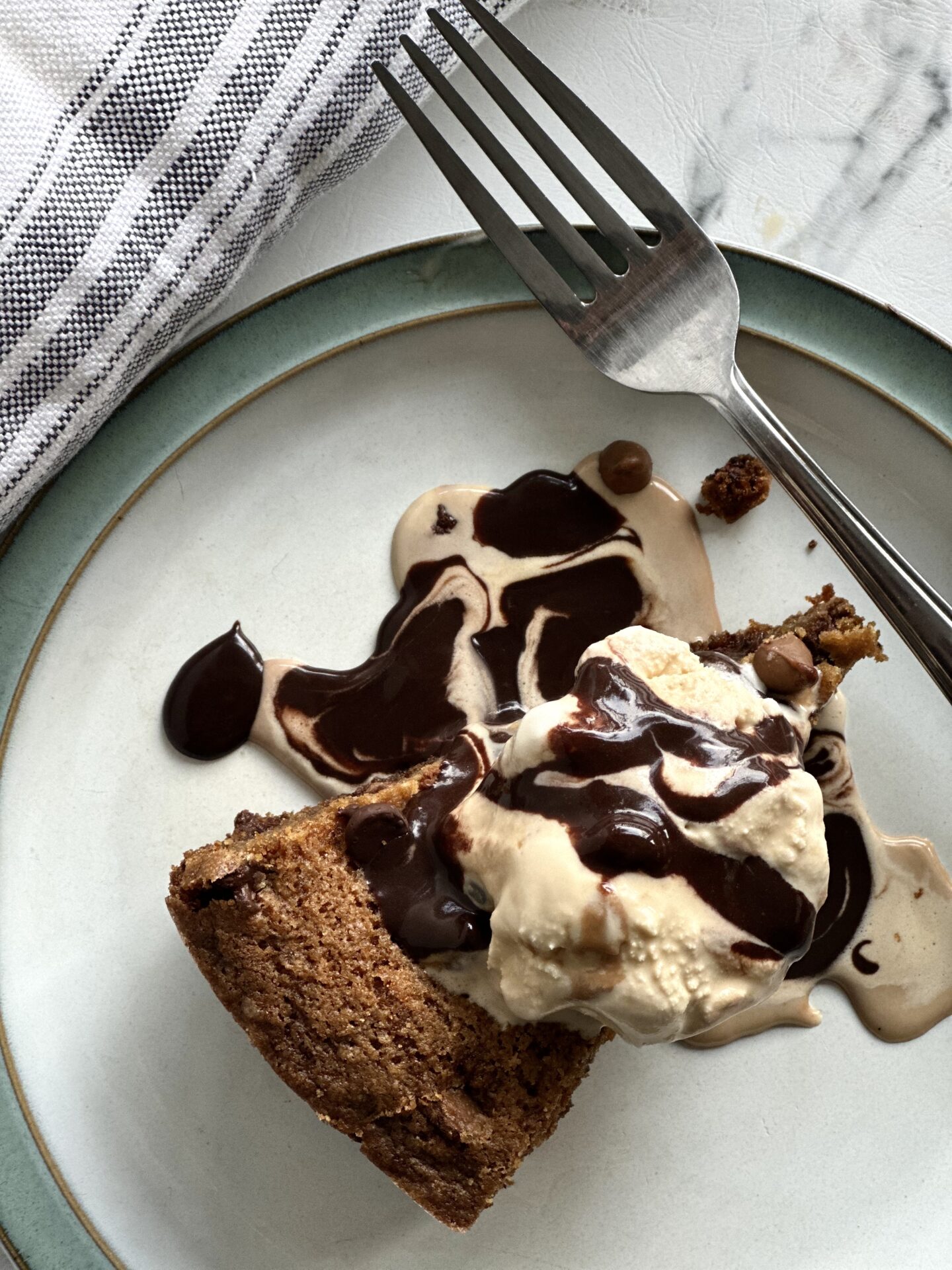 A wedge of a giant deep dish chocolate chip cookie seen from above, topped with caramel ice cream and hot fudge sauce