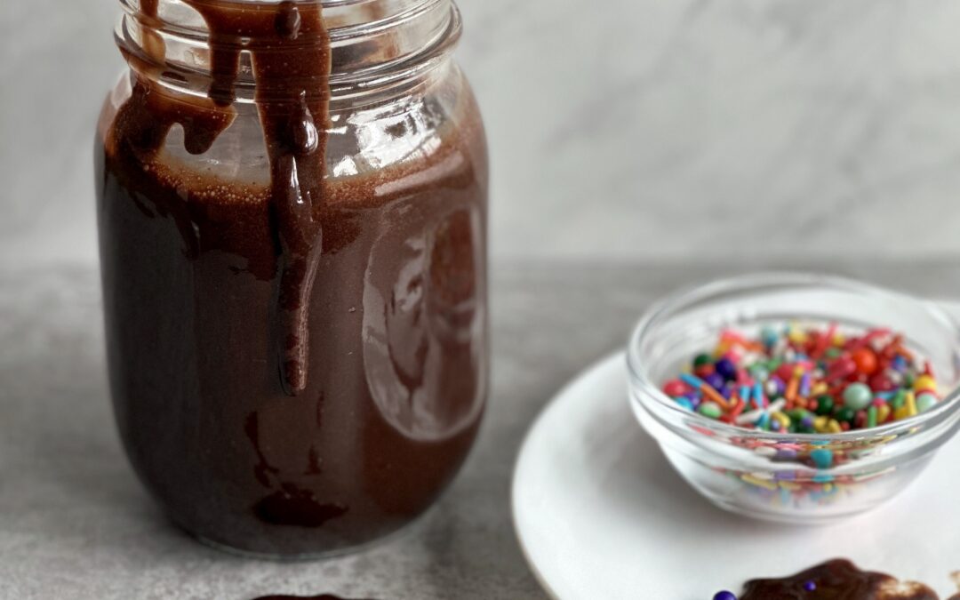 A jar of Hot Chocolate Fudge Sauce with a spoon dripping sauce onto the counter
