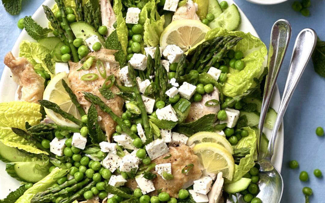 Spring salad with asparagus peas feta and roast chicken displayed on a platter surrounded by lemon mint and a bowl of dressing