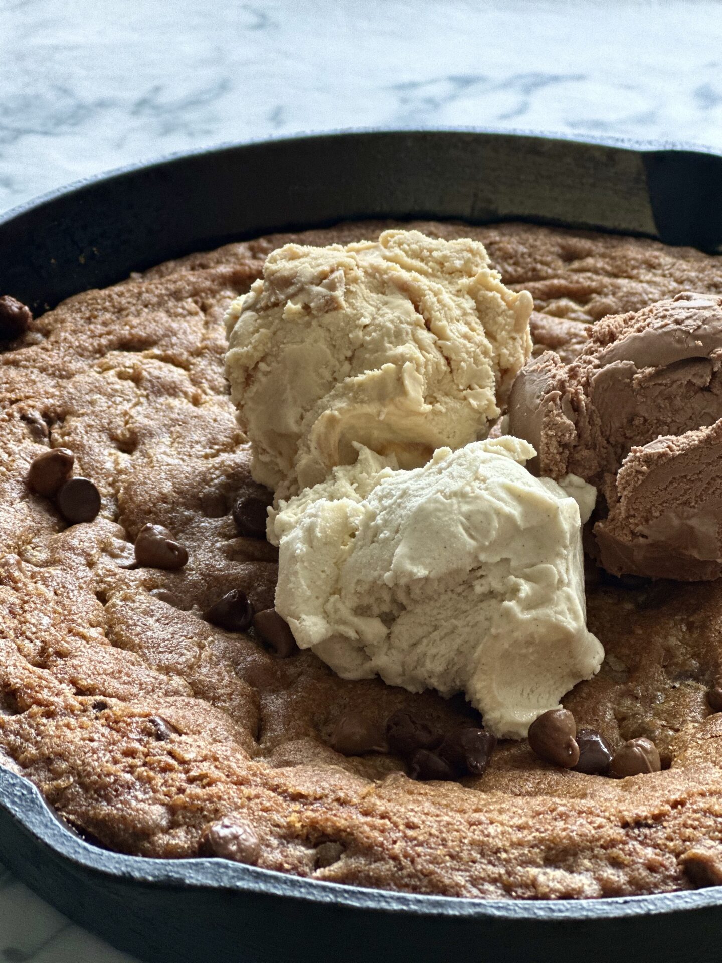 Cast iron pan full of a giant chocolate chip cookie, topped with scoops of vanilla, chocolate and caramel ice cream