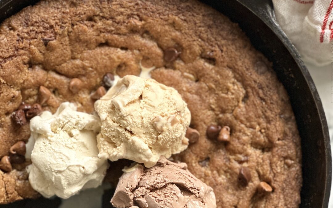 Giant deep dish chocolate chip cookie baked in a cast iron skillet and topped with scoops of ice cream.
