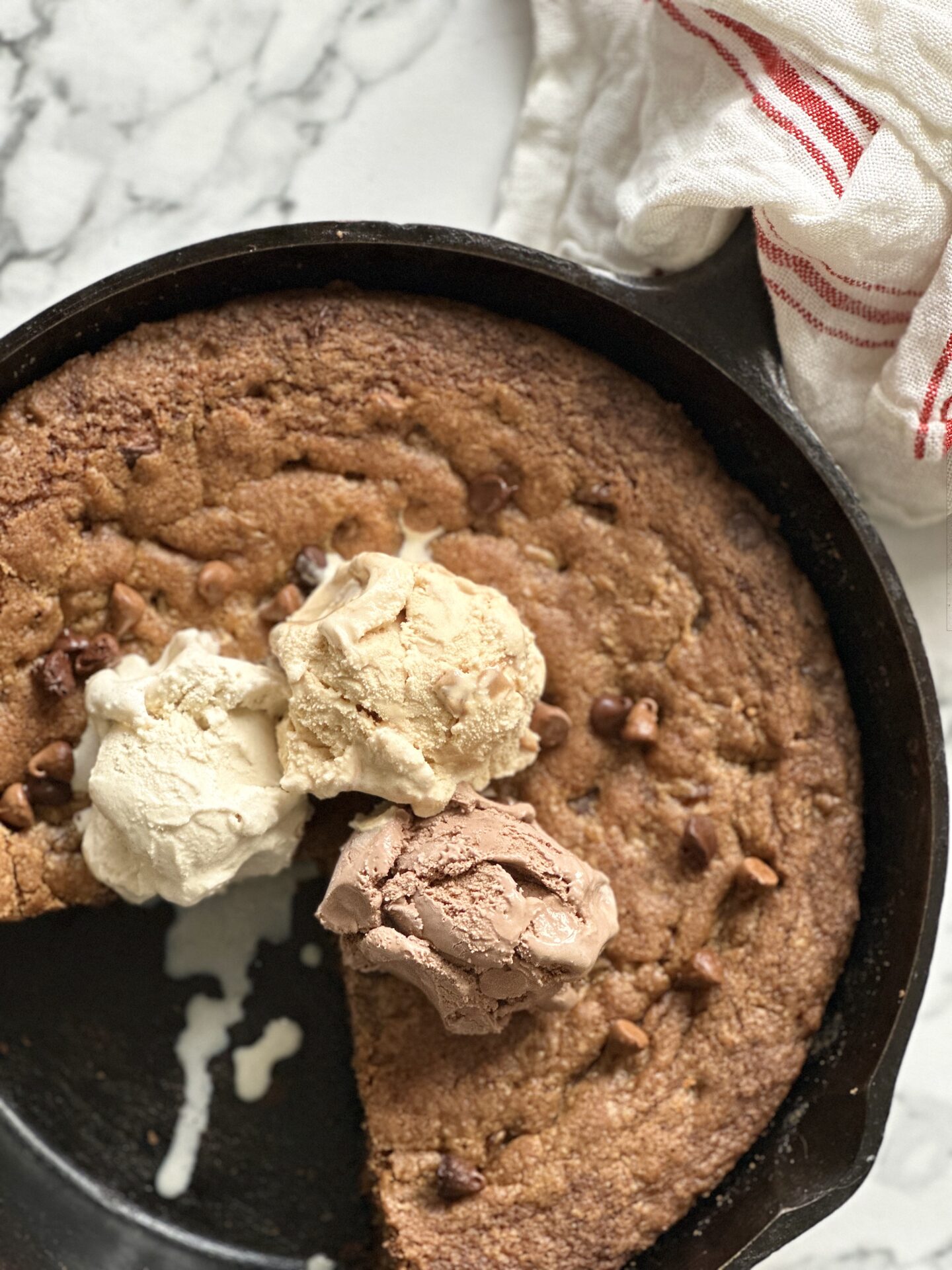 Giant deep dish chocolate chip cookie baked in a cast iron skillet and topped with scoops of ice cream.