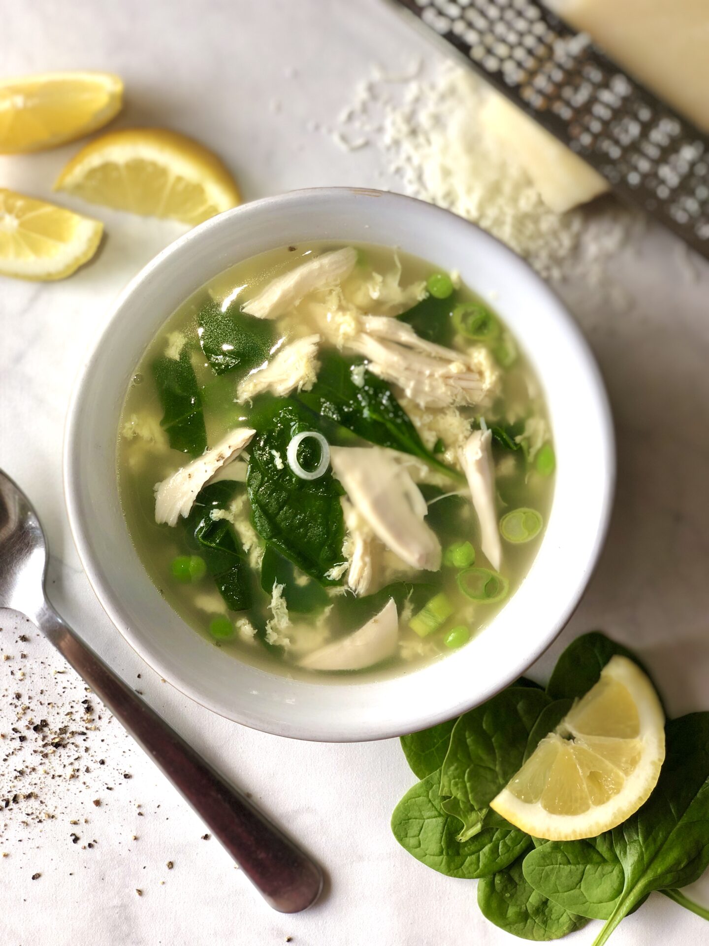 Bowl of spring straciatella soup with chicken and vegetables, with lemon wedges and freshly grated parmesan cheese.