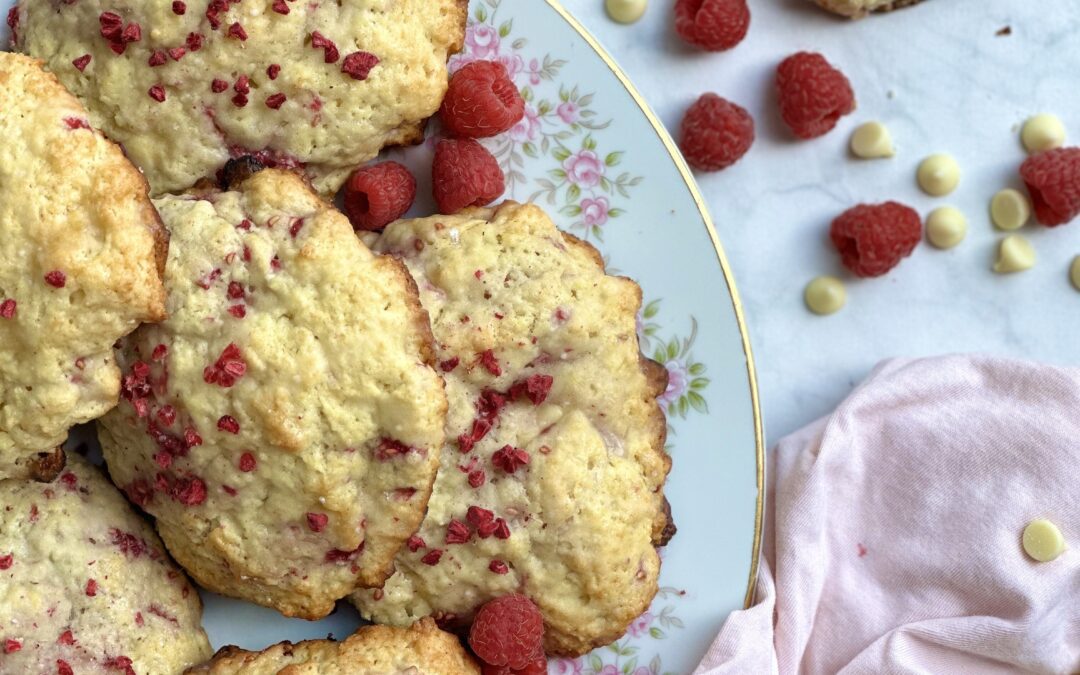 Vintage china plate with pink rosebuds piled high with freshly baked Raspberry White Chocolate Scones, surrounded by fresh red raspberries and white chocolate chips