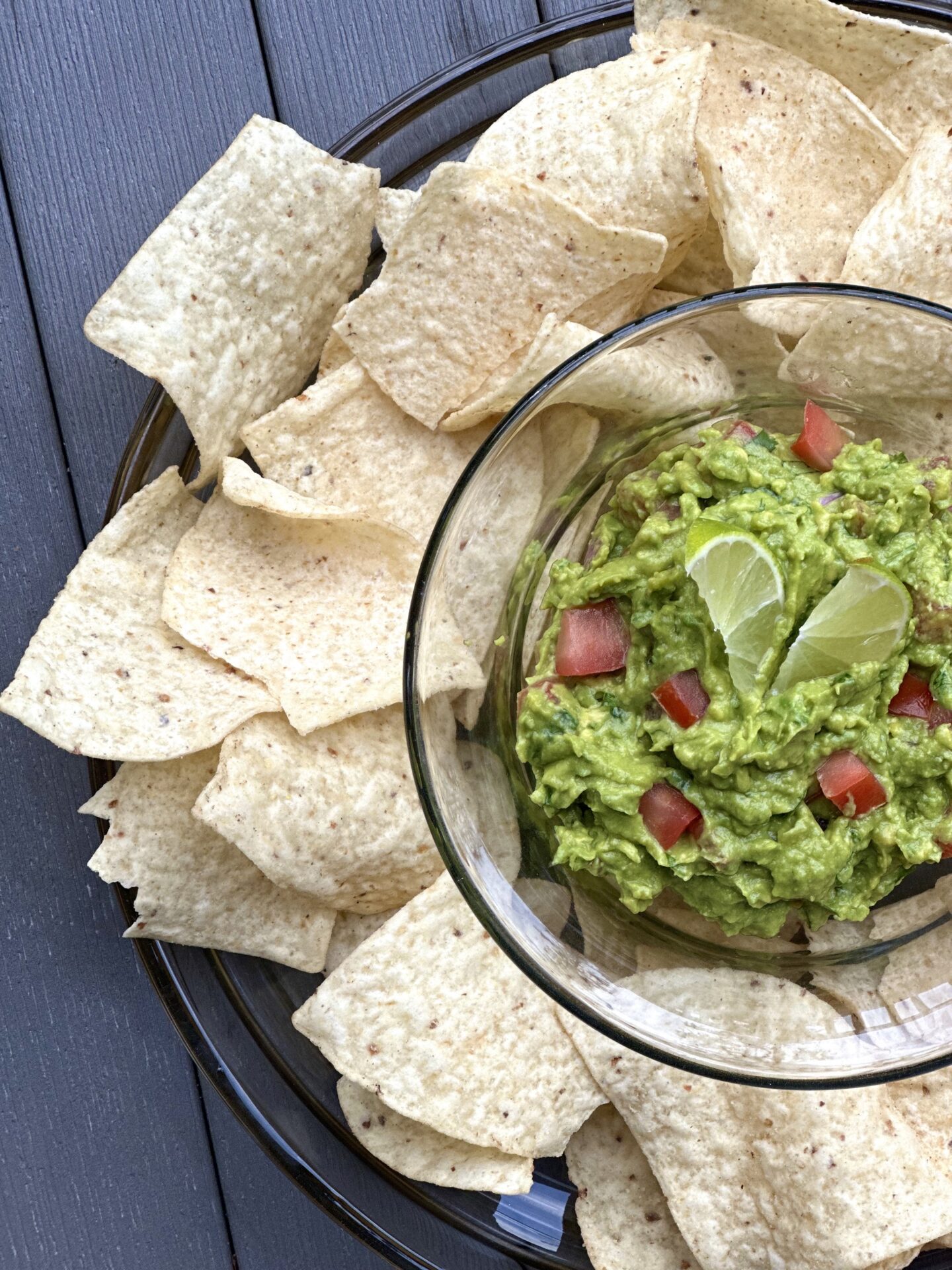  A platter of chips and fresh homemade guacamole sitting on an outdoor patio table, seen from above.