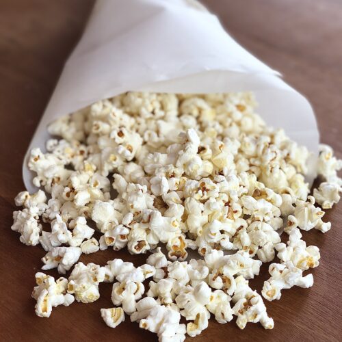 Paper cone of truffle popcorn spilling out onto a wood table