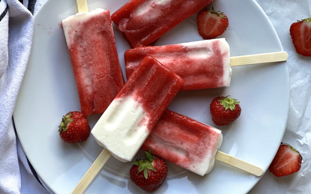 Plate of strawberries and cream breakfast popsicles surrounded by fresh strawberries.