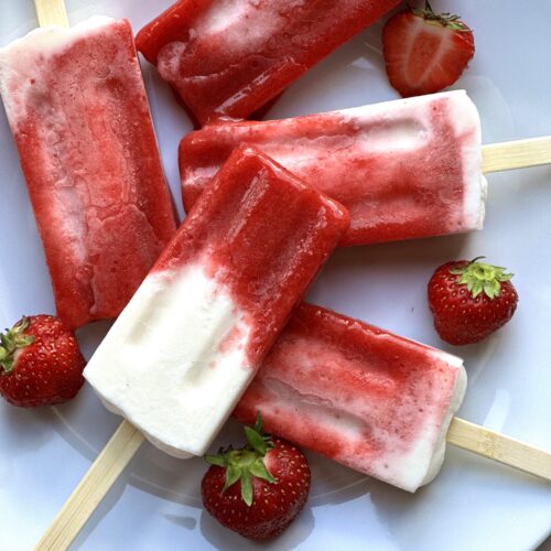 Plate of Strawberries and Cream breakfast popsicles surrounded by fresh strawberries